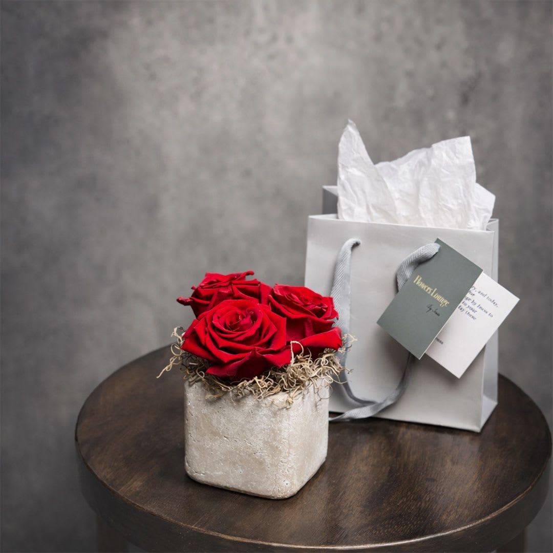Trilogy of Love - A refined arrangement of preserved red roses set in a modern stone vase with natural moss detail, presented with an elegant gift bag. Designed to last, this piece symbolizes love, passion, and timeless beauty. This is a preserved arrangement and does not require water or maintenance. Perfect for romantic gestures and meaningful occasions. Custom greeting card included.