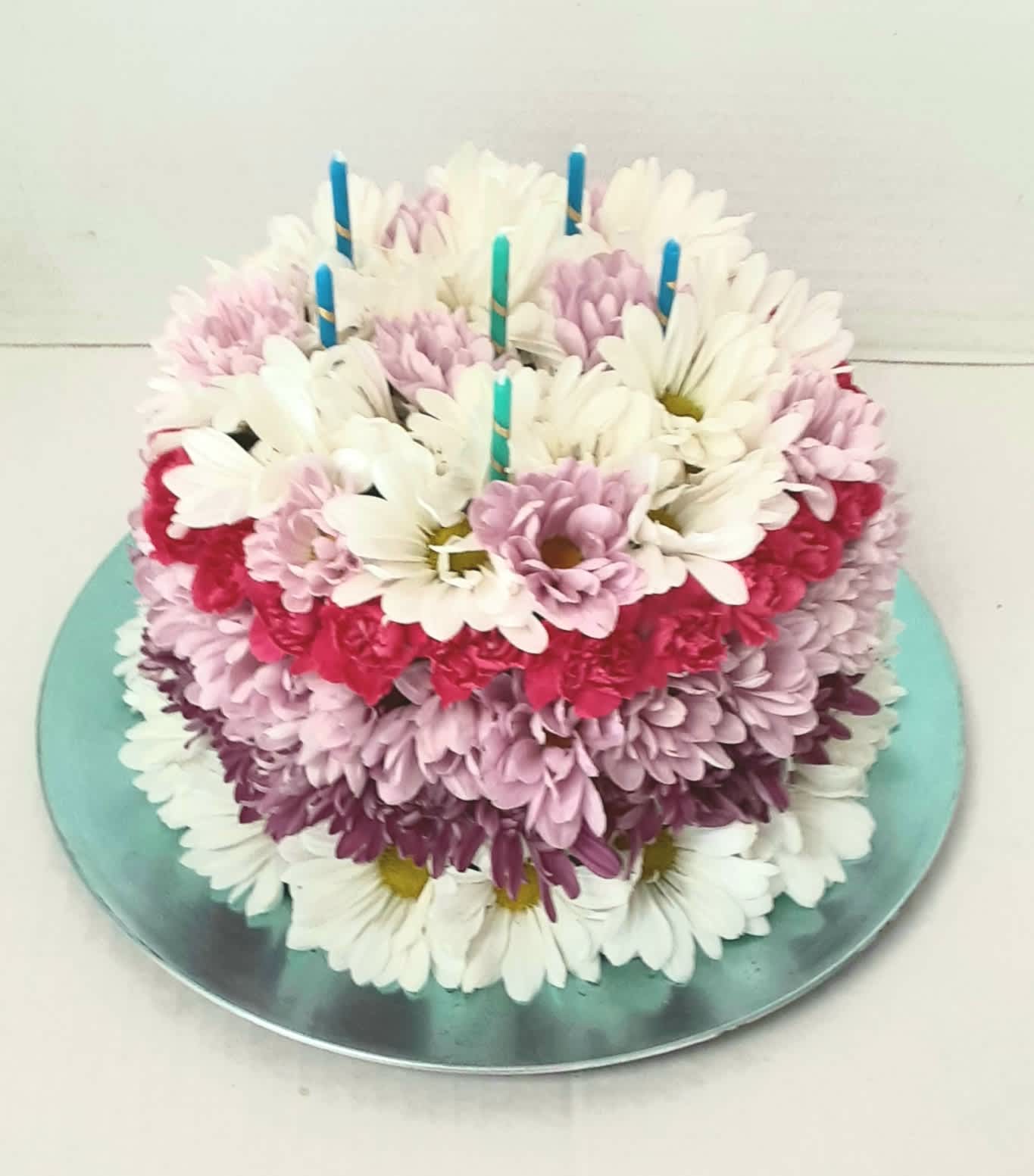 Round cake covered with white, pink, and purple daisies and candles on top