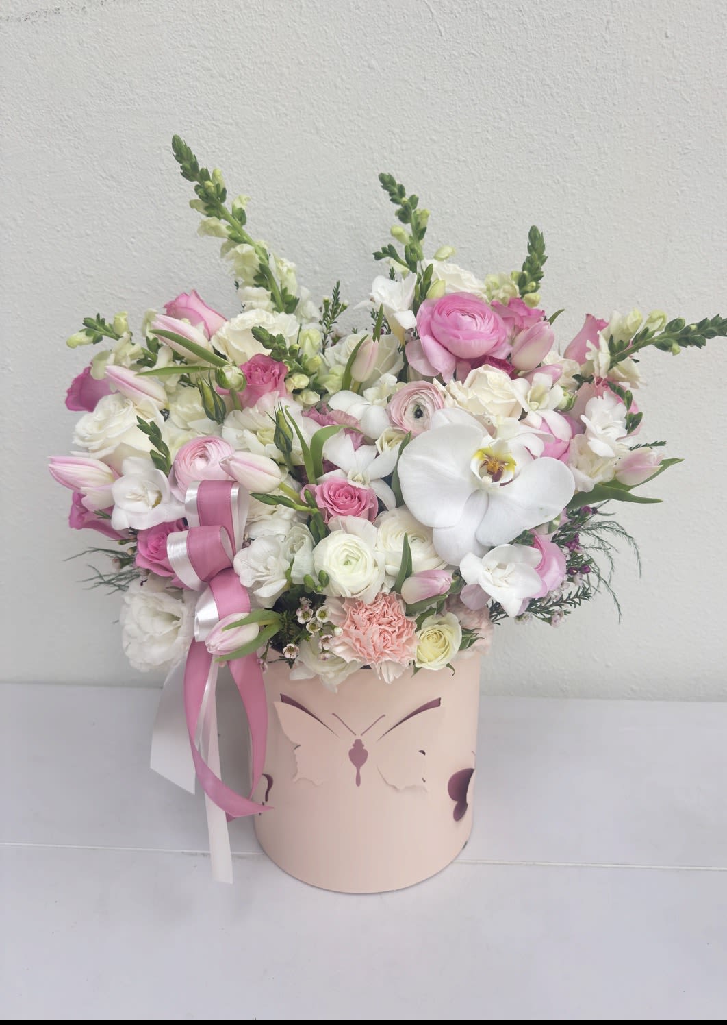 Blush Romance Orchid Box - This elegant flower box features a soft blush palette with delicate pink and white tones, creating a refined and romantic look. Designed with lush blooms and a signature orchid accent, the arrangement feels airy, graceful, and truly luxurious. The composition is full yet balanced, making it a perfect statement piece for any special occasion.  Ideal as a gift for a girlfriend, wife, or someone you want to impress, this arrangement expresses tenderness, beauty, and thoughtful attention. The hat box design adds a modern, upscale touch, making it both stylish and memorable.  Perfect for Valentine’s Day flowers Los Angeles, this arrangement is available for same day flower delivery Los Angeles from a trusted Hollywood florist. A beautiful choice for those looking for flowers in a box and luxury flower delivery Los Angeles.