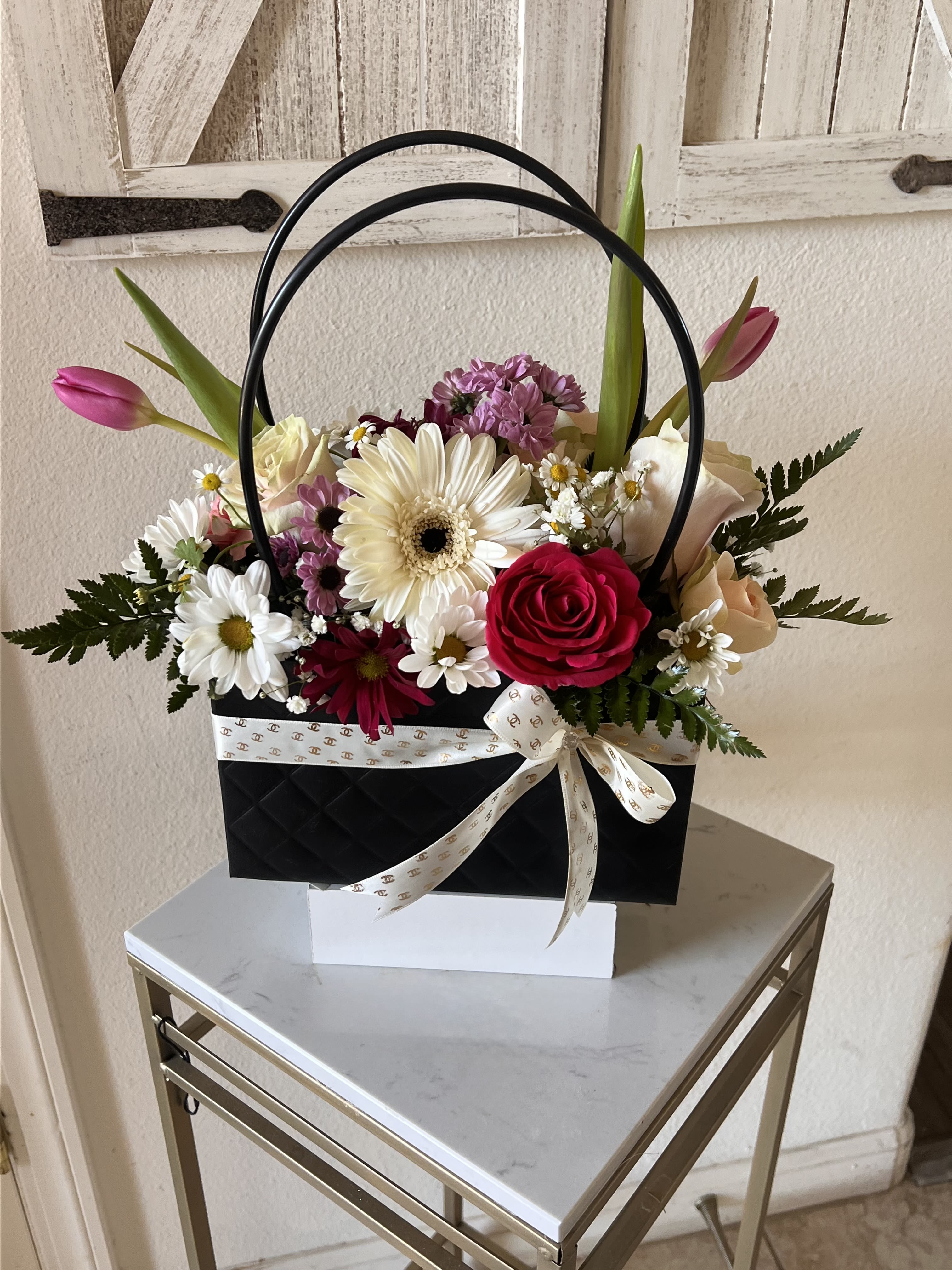 Luxe Love Purse - Make a bold statement with the Luxe Love Purse, a high-fashion floral arrangement designed for those who appreciate the finer things. This designer-inspired gift features a lush, vibrant bouquet of premium seasonal blooms and architectural greenery, meticulously styled to create a look of modern elegance. Housed in a sophisticated quilted black tote with sleek circular handles and finished with a signature ribbon, this chic centerpiece is the perfect "purse" for birthdays, anniversaries, or any occasion that calls for a touch of luxury and romance.