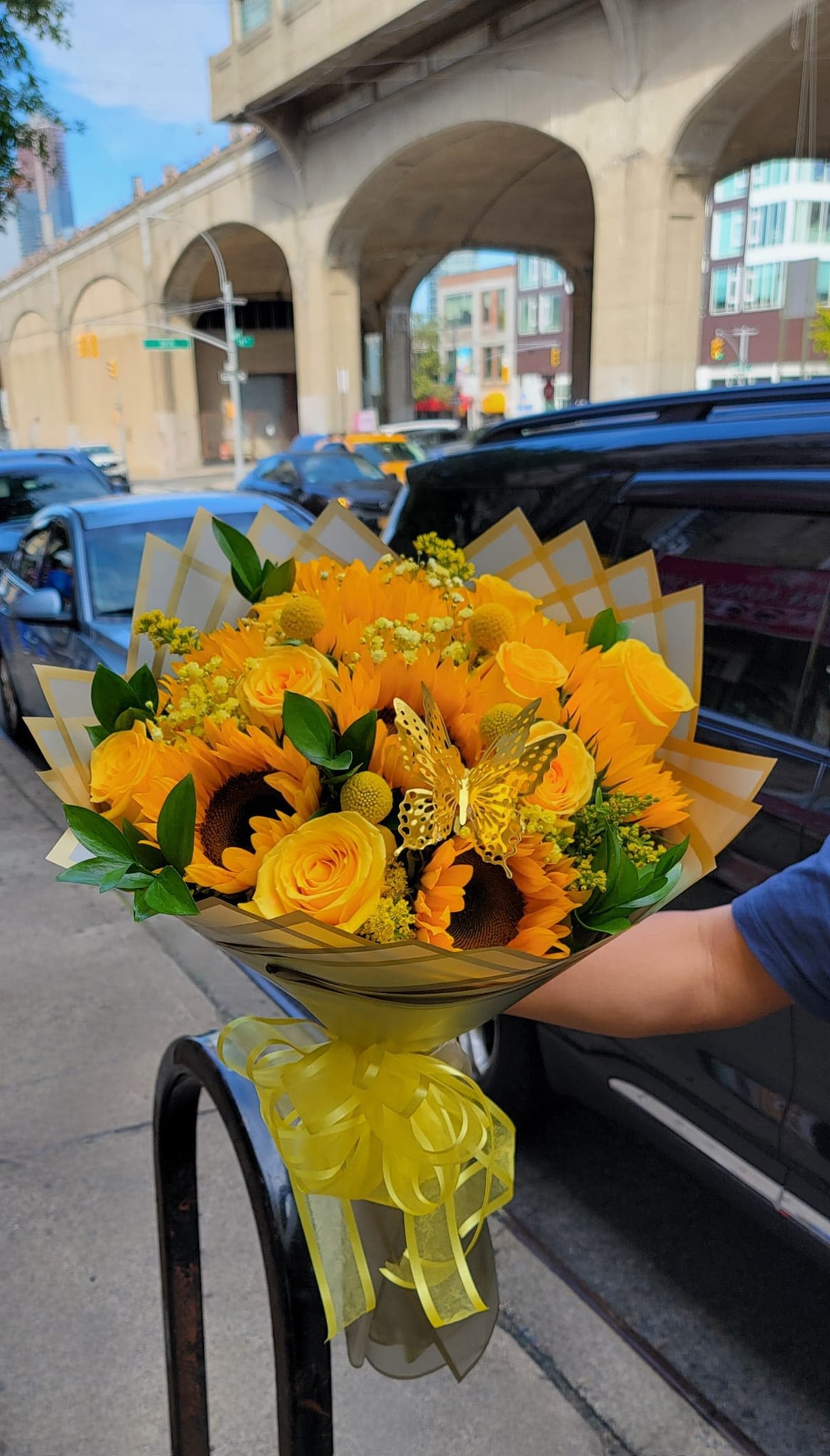 Golden Star - This wonderful wrap bouquet consists of yellow roses, sunflowers, baby breath, and more. All of these flowers are wrapped in gold paper and tied off with yellow ribbon. Decorated with gold butterflies.