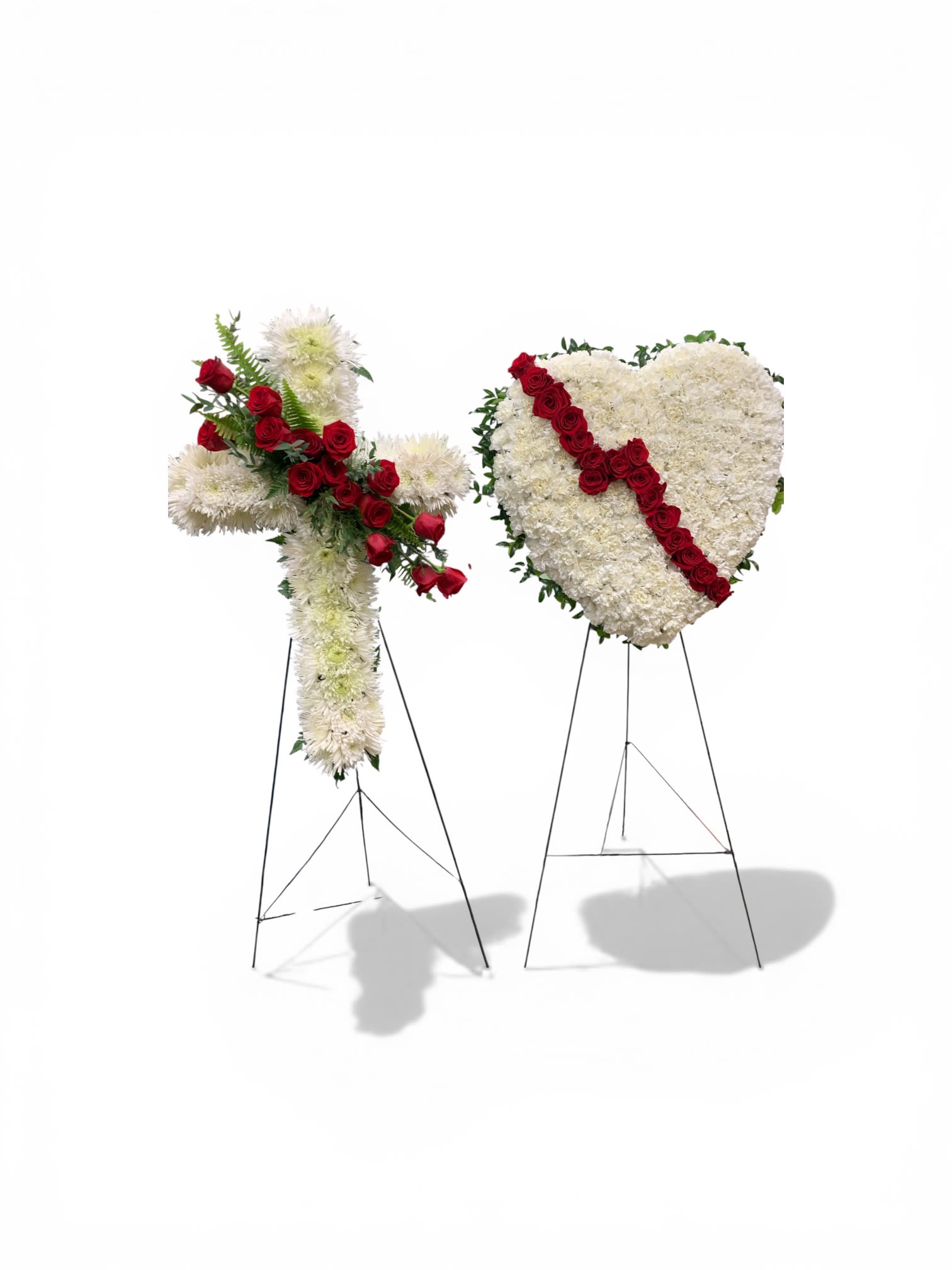 Broken Heart and Cross - A white floral cross and matching white heart, each mounted on a slender metal easel, create a dignified sympathy arrangement that honors faith and memory. The standing sympathy pieces-one cross accented with a diagonal spray of red roses and one solid white heart crossed by the same bold red band-speak plainly to funeral and memorial services while offering a visual focus for remembrance.  Crafted from white chrysanthemums and carnations as the background with clusters of red roses for the diagonal accents, the arrangements feature a subtle green edging that defines the heart's silhouette and softens the overall palette. Both pieces are densely arranged for a full, polished look and arrive ready to display on their included metal easels; they may be ordered together or separately to suit the service or graveside setting.  These designs are meant to comfort the grieving and mark a sacred moment-the cross communicates faith and the heart expresses enduring love, making them appropriate for a religious service, memorial, or funeral. For size options or to request a single piece rather than the pair, please call our shop and we'll help arrange delivery and placement details.