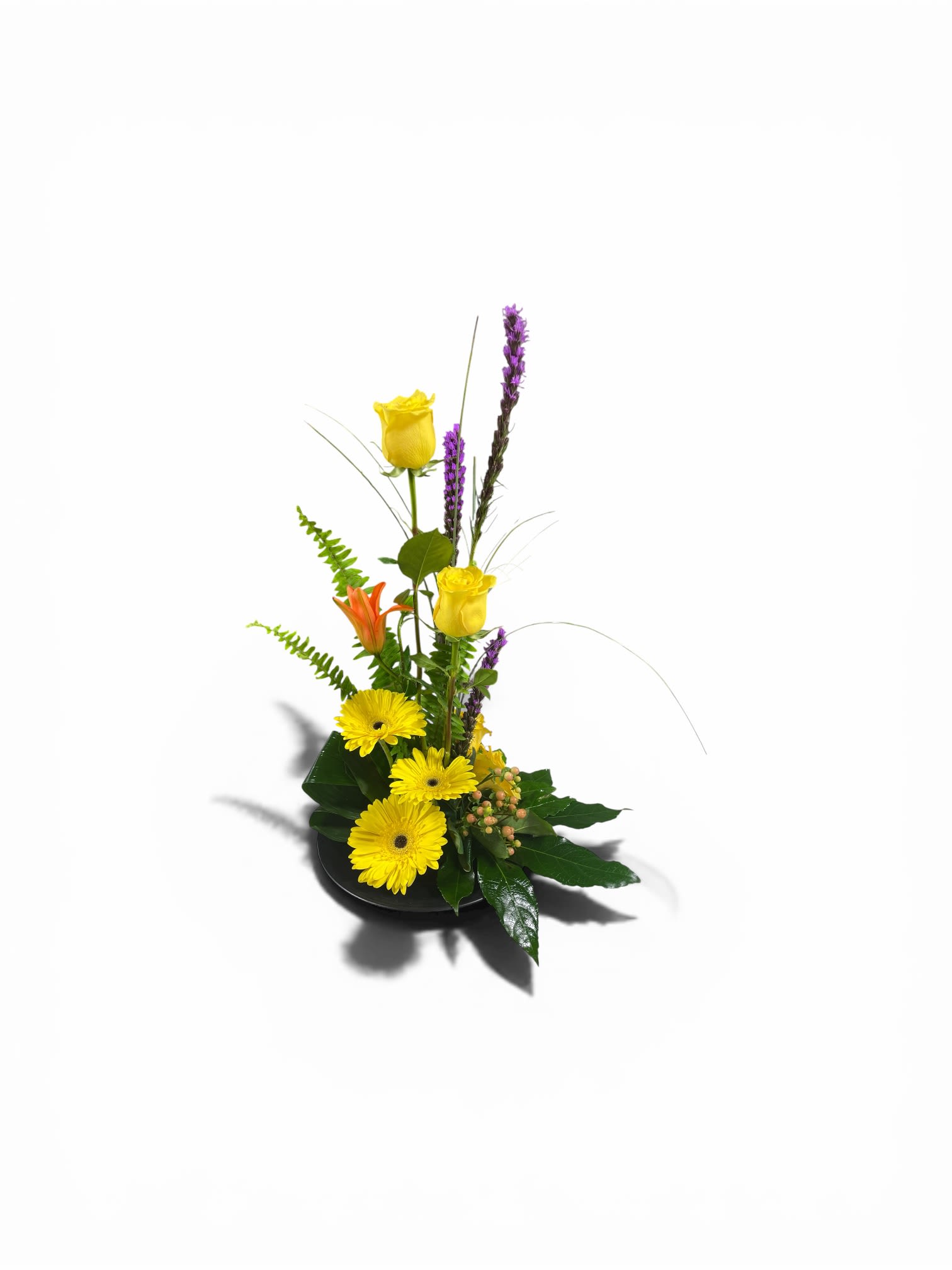 Lanie's Yellow Laughter  - Sunny yellow gerbera daisies and a pair of upright yellow roses create an immediate burst of cheer in this flower arrangement-perfect as a birthday bouquet, a get well gift, or a thinking-of-you surprise. Lanie's Yellow Laughter brings a modern, energetic vibe that also suits Mother's Day, a springtime Easter table, or a bright addition to anniversary and housewarming celebrations; the recipient will feel genuinely uplifted by its joyful color story.  A single orange Asiatic lily bloom and slim purple flower spikes add striking contrast and vertical movement, while small berry clusters introduce texture against a low, glossy black ceramic dish. The compact design balances a lively, contemporary silhouette with easy display-ideal for desks, bedside tables, or kitchen islands. Size and care: designed as a low centerpiece, refresh water daily and trim stems every few days to keep blooms looking their brightest.