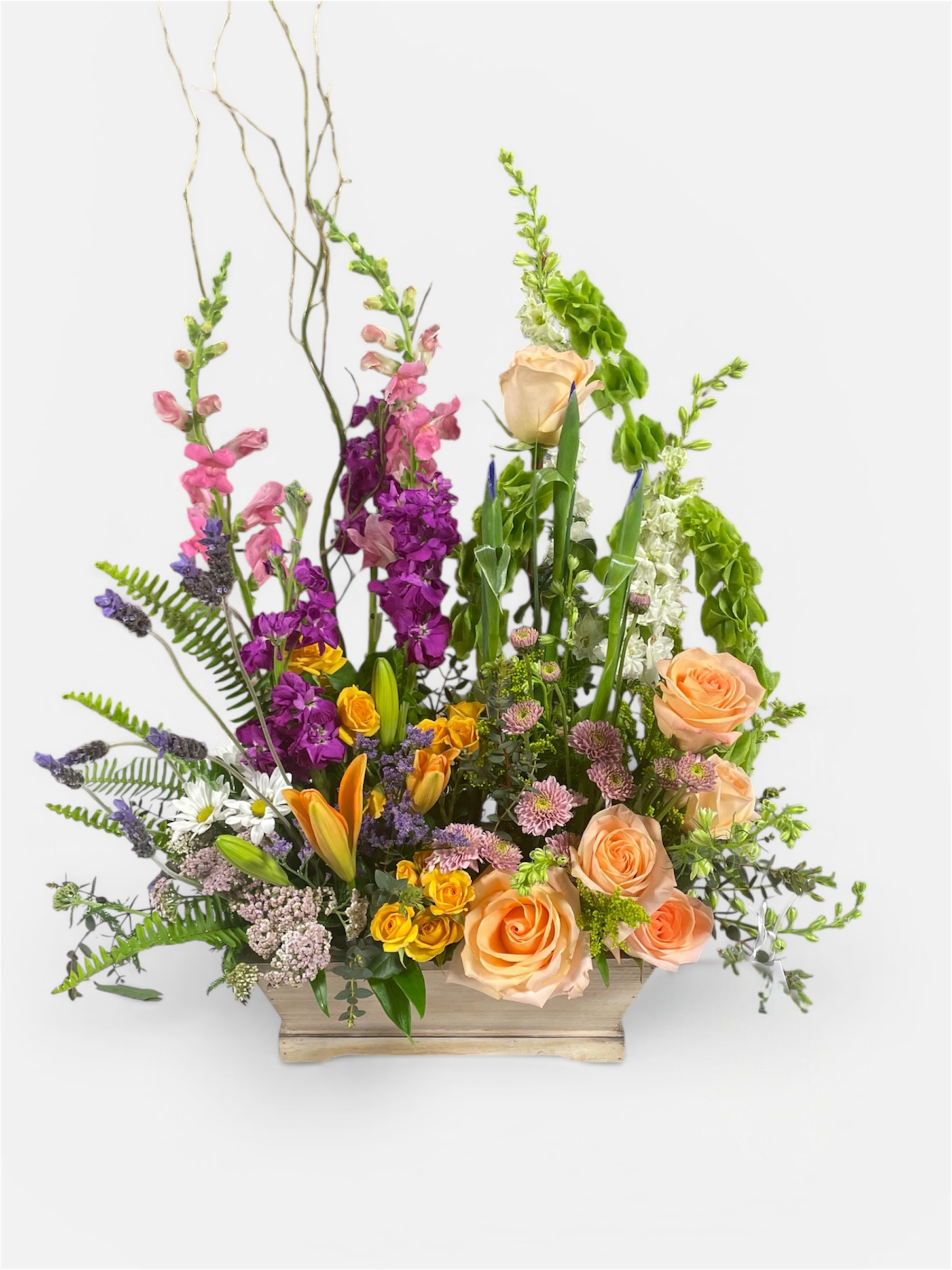 Colorful mixed arrangement of peach roses, yellow lilies, and purple flowers in a wooden box.