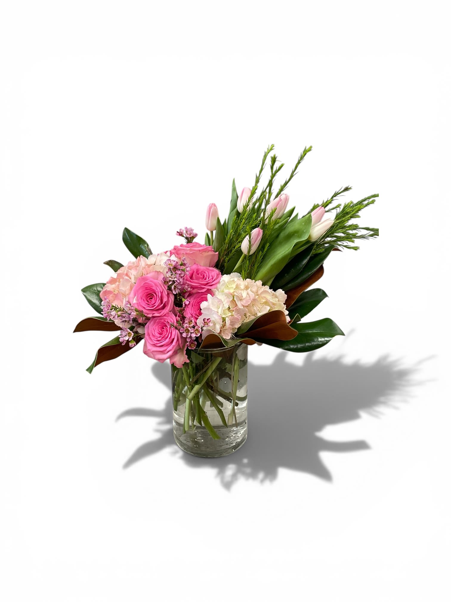 Arrangement of pink roses, pale tulips, and blush hydrangeas in a clear glass vase