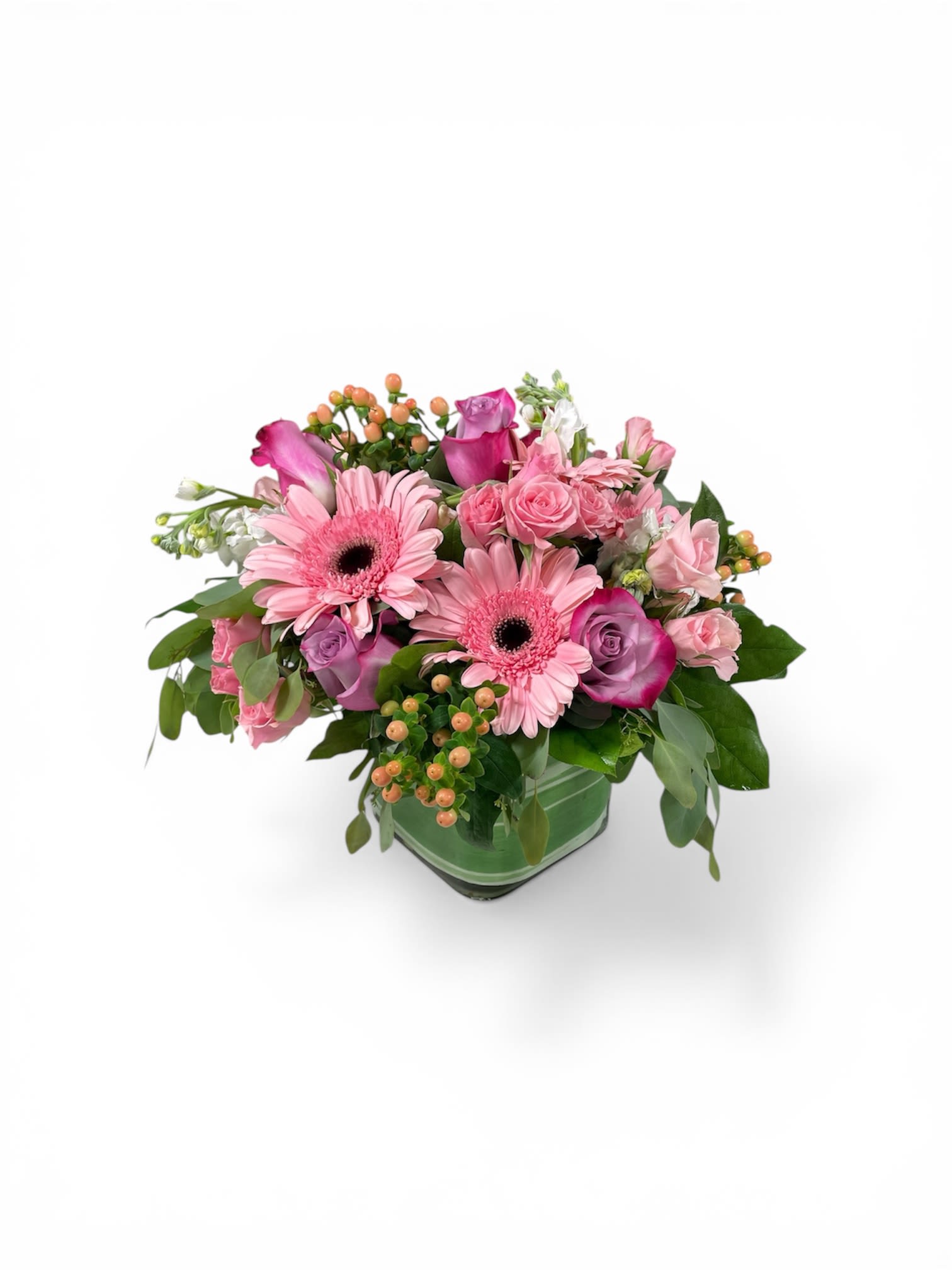Pretty in Pink Petal Perfection Style  - Large pink gerbera daisies take center stage in this pretty-in-pink flower arrangement, making it an ideal birthday bouquet, Mother's Day gift, or sweet "thinking of you" surprise. The rounded, compact design and soft palette of pinks, purples, peaches, and white give the arrangement a cheerful, affectionate feel that also suits anniversaries, get-well wishes, new babies, or a simple just-because moment.  This Petal Perfection style arrangement pairs pink and lavender roses with spray roses, creamy white stock, and delicate clusters of peach berries for texture. The blooms are arranged low and lush in a green glass cube vase that lends modern elegance and stability-perfect for tabletops, desks, or a kitchen counter. Size and care: delivered ready-to-display in its vase; keep in fresh water, out of direct heat, and trim stems slightly if needed to extend vase life.