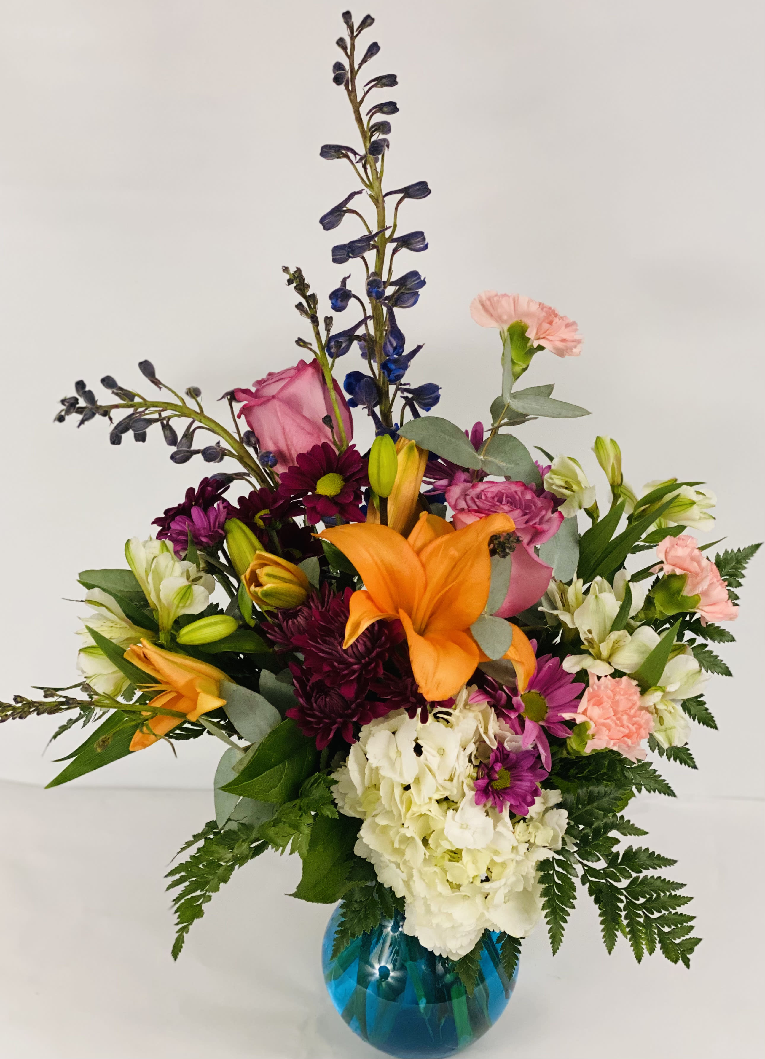 Mixed bouquet in a blue glass vase with orange lilies and pink flowers