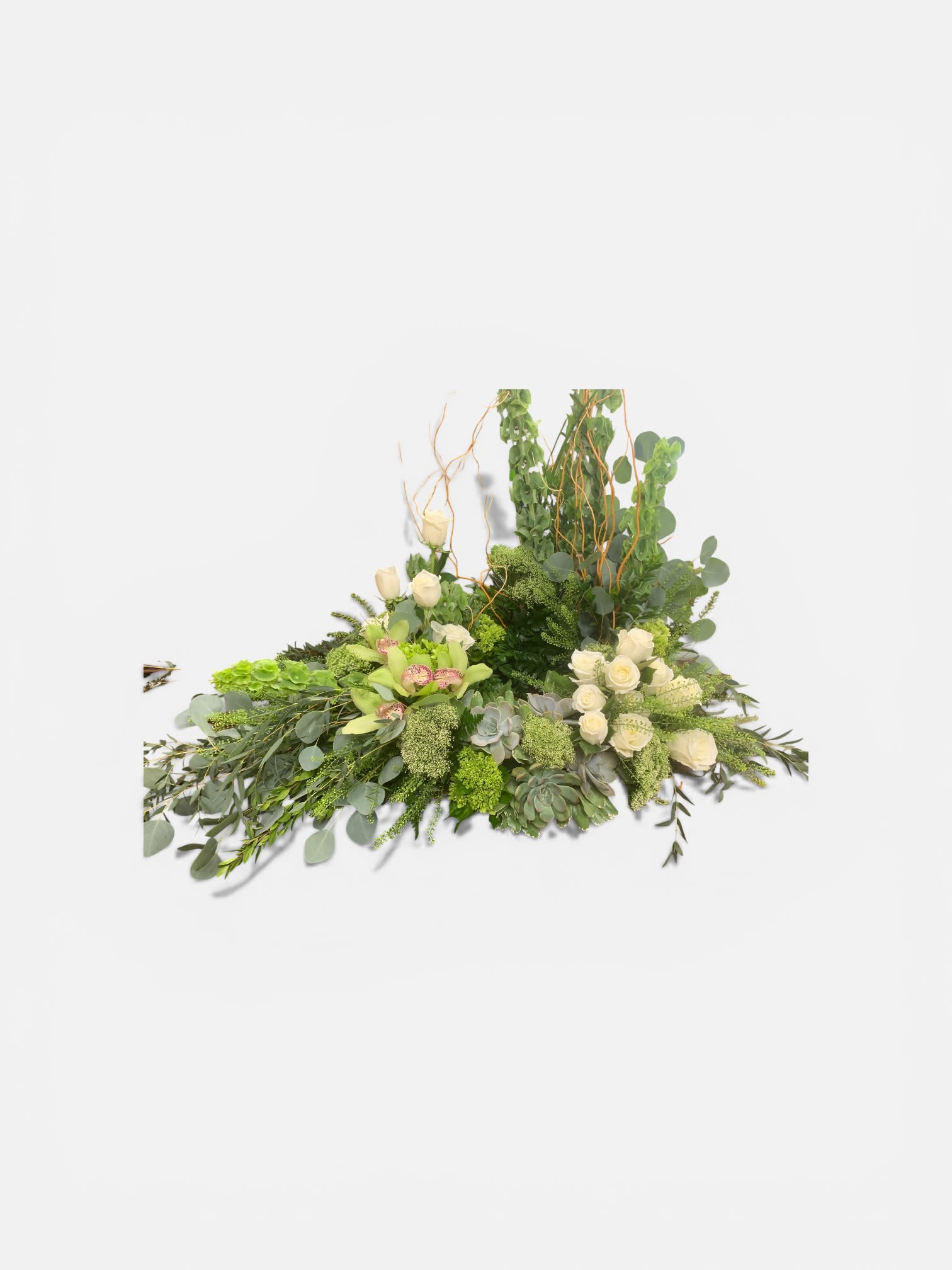 Nature‘s Own Cremation Wreath  - A long, low cremation wreath that brings a calm, natural presence to sympathy and funeral settings - the kind of arrangement that helps the person you're honoring feel quietly seen. Clusters of creamy white roses and green cymbidium orchids form the soft focal band, while succulents and textured green blooms weave a layered, organic look that reads both gentle and sculptural.  Taller vertical stems and curly branches rise at one end to create a modern, asymmetrical silhouette that works well as a memorial centerpiece or a subdued statement on a console or chapel table. The green, white, and soft pink palette keeps the design serene and versatile; the mix of smooth orchid petals, velvety roses, and the fleshy texture of succulents gives visual interest up close and from a distance.  Arrives ready to place with a low profile designed for cremation or tabletop display. For care: keep away from direct heat and replace water as needed for any conditioned stems; succulents are arranged to retain form and require minimal attention. This wreath is a thoughtful way to offer comfort and quiet beauty during a difficult time.