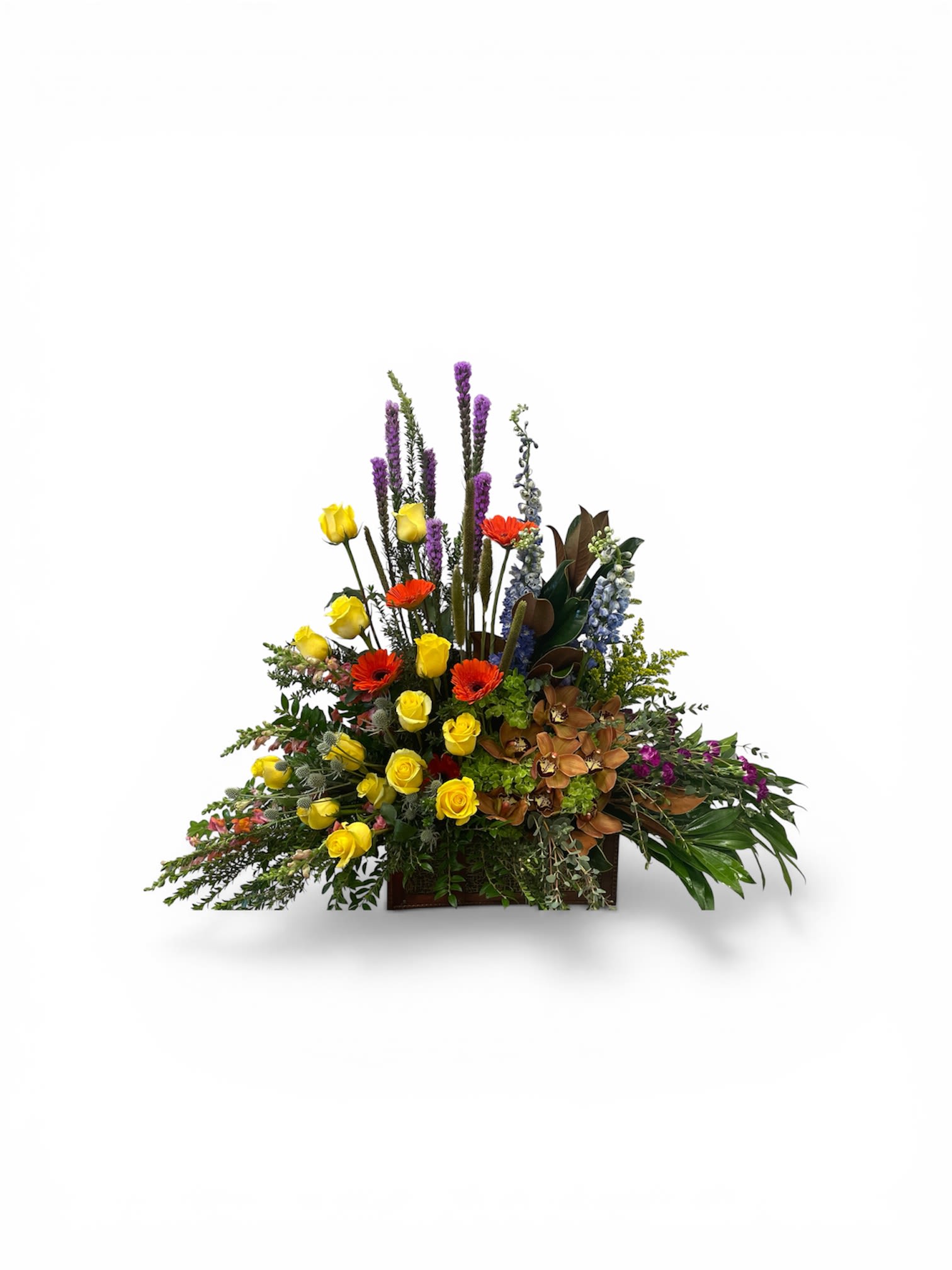 Seasons in Bloom  - A joyful burst of color that feels like a sunlit garden in a wooden box - this low, wide flower arrangement is a mixed-color floral gift perfect for a birthday bouquet, Mother's Day surprise, get well wishes, or a bright Easter centerpiece. The Seasons in Bloom arrangement presents a cheerful, celebratory mood that makes the recipient feel seen and celebrated, whether you're saying "congratulations," "thinking of you," or "happy anniversary."  Dense clusters of yellow roses and vibrant orange gerbera daisies form the warm heart of the design, while tall purple delphinium spikes and vivid blue stems rise through the center for vertical contrast and drama. Caramel-toned orchids and other mixed blooms create a rich focal area on one side, and fresh greenery softens the edges-arranged in a rectangular wooden box that lends a structured, garden-fresh look suitable for housewarming, graduation, sympathy, or holiday gifting. The arrangement is offered seasonally in spring, summer, fall and winter palettes; sizes and care details are available at checkout to help this cheerful centerpiece arrive ready to brighten their day.
