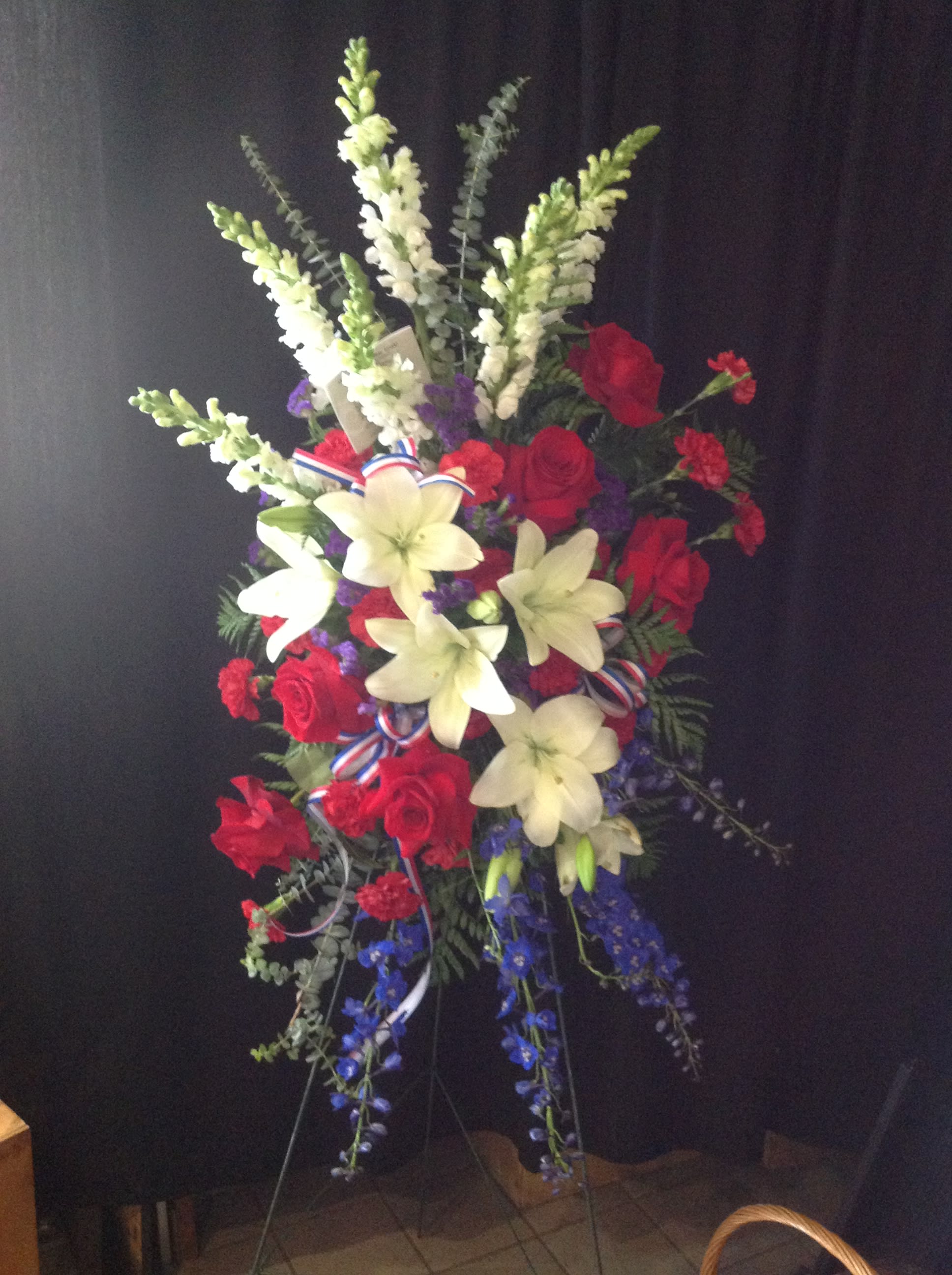 Red, White, And Blue  - Standing Spray available in varying colors and styles. Please call to place order for this specific piece so we can get the look you want. Pictured is our "Patriot" Spray for memorial day or any veteran funeral. Can vary in price depending on flowers and size of arrangement.    *Flowers subject to change based on supply*