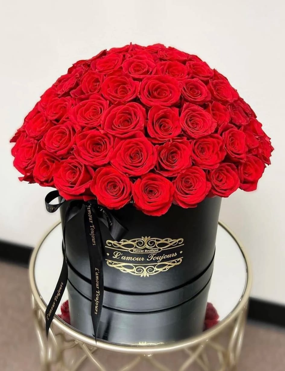 100 Everlasting Roses - Real Roses that last over 3 years - A lush dome of vivid red roses arranged in a sleek black hatbox creates an unforgettable romantic statement-perfect as a Valentine's Day bouquet or to mark an anniversary or other intimate milestone. The densely packed canopy of preserved real roses reads as endlessly abundant in the glossy mirrored reflection, so the person you're thinking of will feel seen, celebrated, and deeply cherished the moment they set eyes on it.  These are preserved Ecuadorian roses treated to last over three years while keeping the natural texture and softness of fresh blooms. The arrangement sits in a polished black hatbox with gold lettering and a black satin ribbon for a refined, gift-ready presentation; shown here on a round mirrored table to highlight its dramatic presence. Zero maintenance is required-no water or trimming-making it an easy, long-lasting reminder of your affection that keeps giving beautiful color and form year after year.