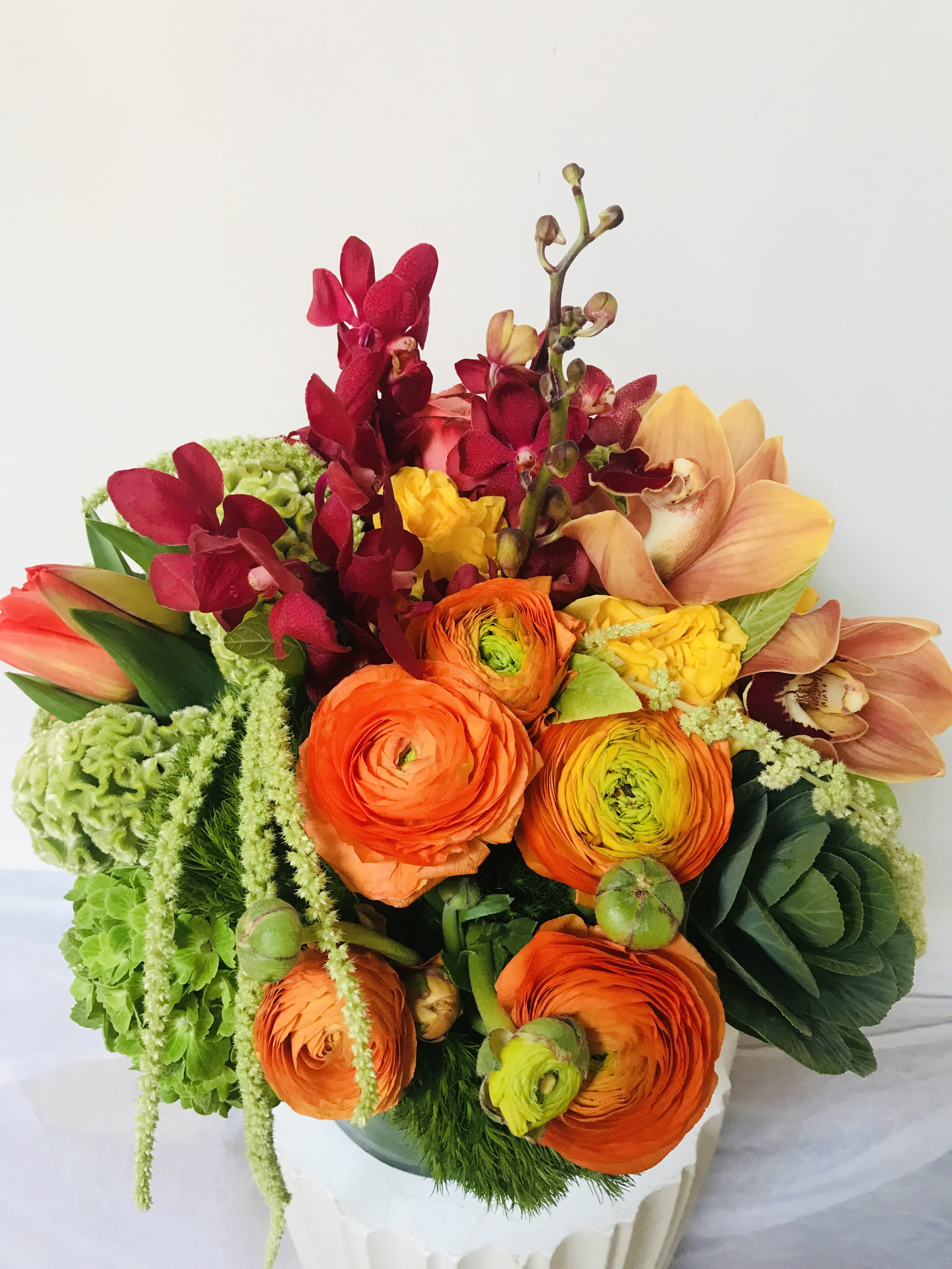 La La Land - Introducing La La Land by Jane's Roses, a vibrant and luxurious floral arrangement perfect for any occasion. This exquisite design, crafted by a premier San Francisco Florist, captures the city's lively spirit with a rich tapestry of colors and textures.  The bouquet features dramatic, deep crimson Mokara Orchids and exotic salmon-to-peach Cymbidium Orchids, adding a touch of sophisticated drama. The focal point is a cluster of stunning Orange Ranunculus, their layered petals showcasing a radiant sunset hue with bright lime-green centers.  Lush, cascading green textures ground the arrangement, including vibrant green Dianthus, trailing Ambrozia/Amaranthus, and the unique structure of Green Hellebore buds. The inclusion of decorative Kale provides a modern, architectural element.  La La Land is a statement of opulence and joy, ideal for celebrating milestones or simply bringing luxury into your home. Order this unique creation from your trusted San Francisco Florist for guaranteed quality and unforgettable elegance. It’s more than a bouquet—it's an experience.