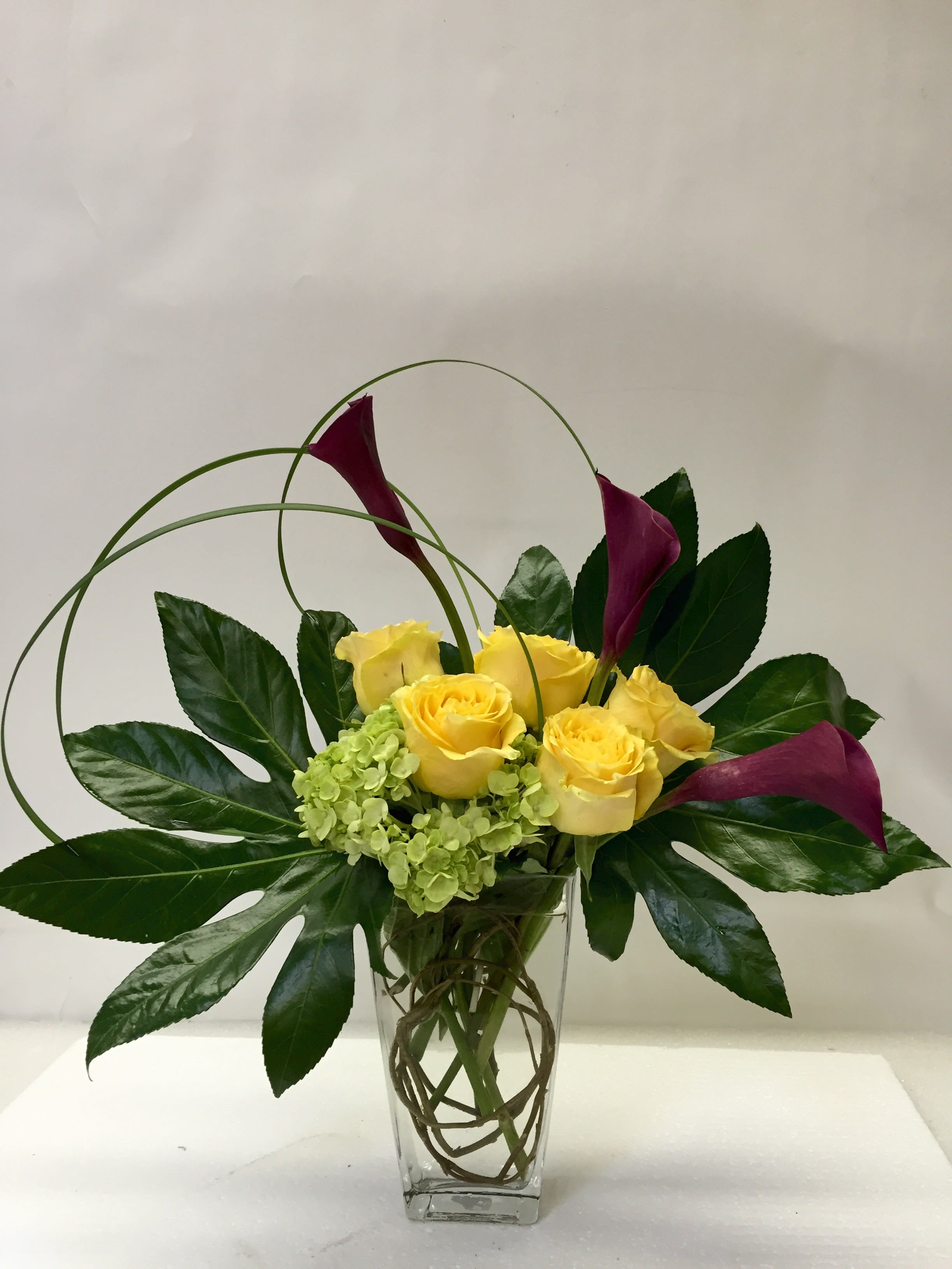 While You Were Sleeping - The Artistic Six: Modern Flower Delivery San Francisco Make a statement with clean lines and bold color! Order flowers online from Jane's Roses to send flowers that showcase contemporary floral artistry, perfect for the modern minimalist or art lover.  This stunning, compact arrangement features:  Six Premium Roses: Your choice of color, showcased here in vibrant yellow for a cheerful, striking look.  Lush Greenery: Dramatic, broad leaves (like Fatsia) and soft green Hydrangea create a vivid, textural foundation.  Modern Vase: Artfully designed in a sleek clear glass vase with unique structural elements (like curly willow and dark Calla Lilies, as shown) that provide height and visual interest.  Trust your local San Francisco florist for unique design and guaranteed freshness.  Same-Day Flower Delivery SF is available! Buy online before 1:00 PM to qualify for fast flower delivery in San Francisco and the Bay Area. Shop this exclusive design now!
