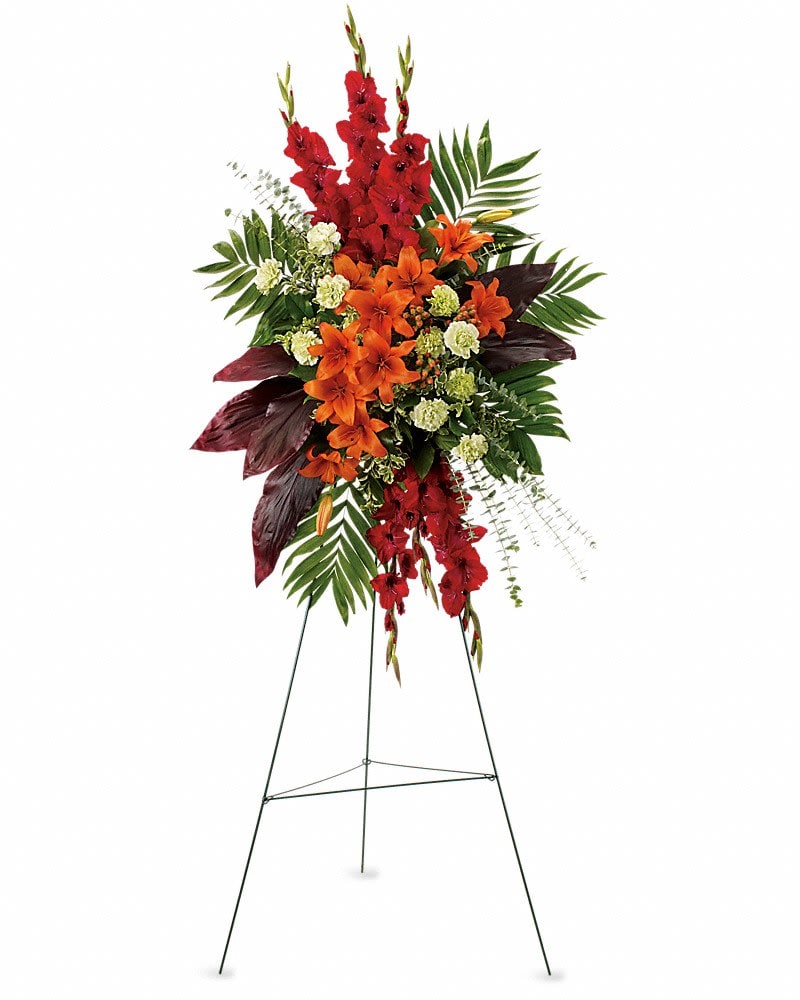A New Sunrise Spray - When a loved one has passed this radiant spray of red and orange flowers will be a reminder of happy times past that will never be forgotten. The stunning arrangement includes orange Asiatic lilies red gladioli green carnations peach hypericum emerald palm and red ti leaves accented with assorted greenery.