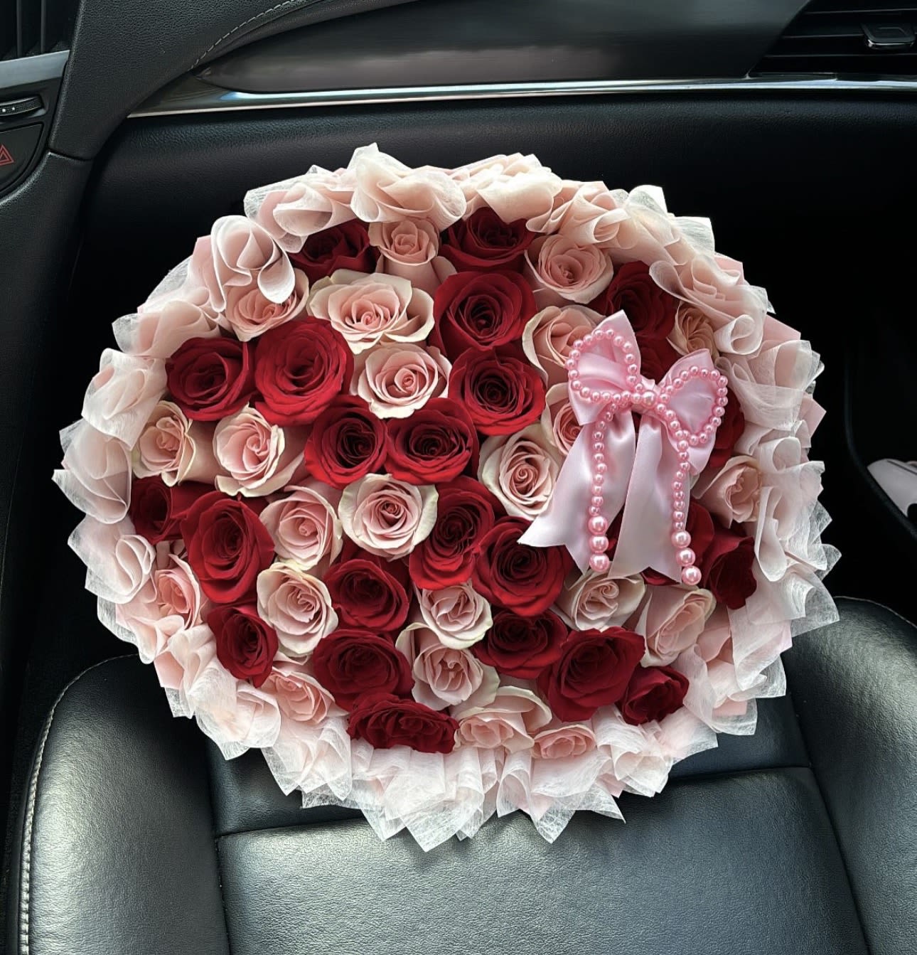 Make her blush - A striking round bouquet crafted with deep red and blush pink roses, symbolizing passion and romance. Wrapped in soft layers of sheer tulle and finished with an elegant pearl-embellished satin bow, this arrangement is designed to make an unforgettable impression.
