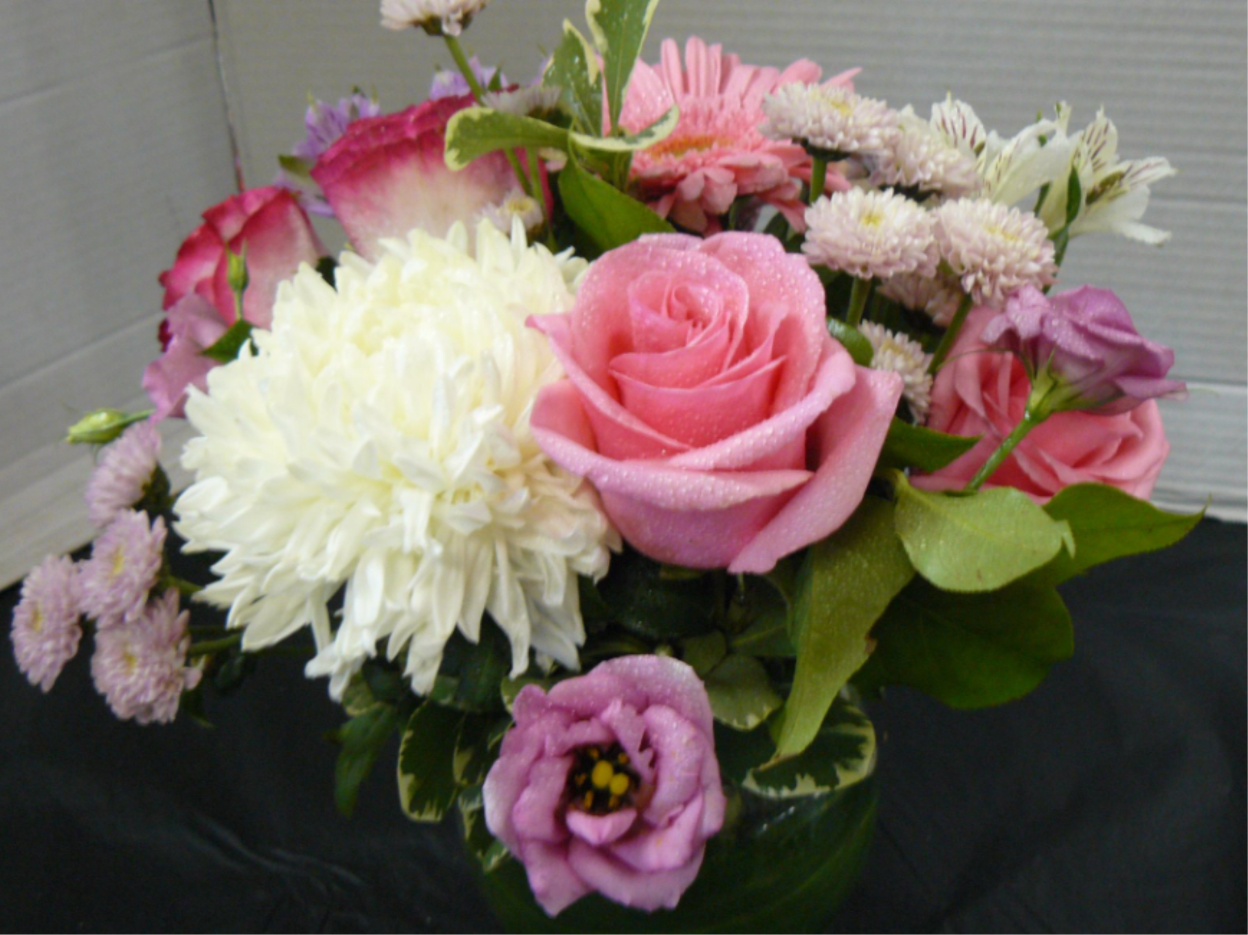 Low glass vase of pink roses, lavender lisianthus, white mum, and mixed pink daisies