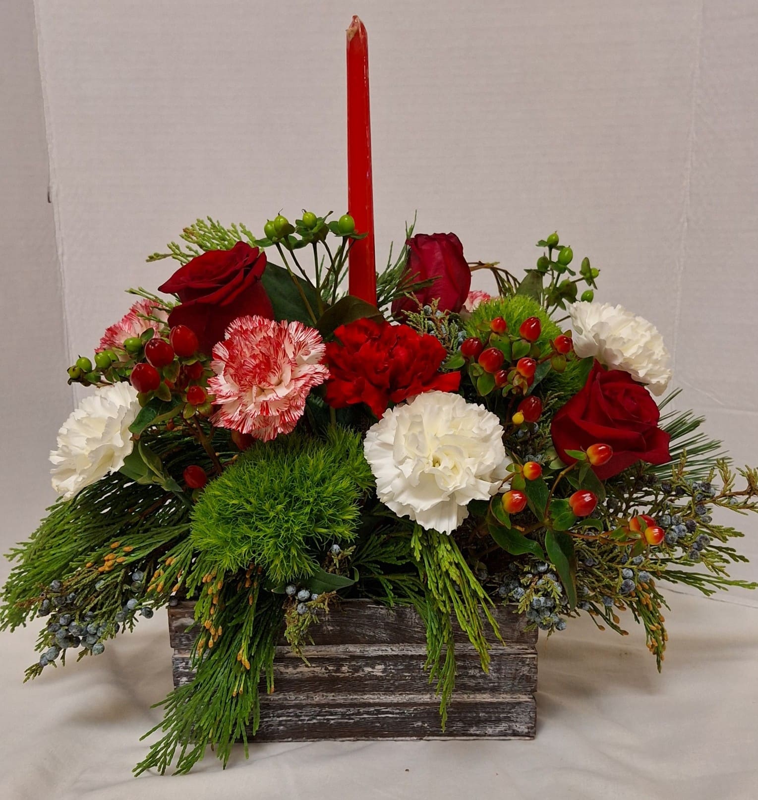 Rustic Holiday - Grey/Black wood panel box, assorted Christmas greens, candy cane carnations, white carnations, red roses and hypericum berries. Finished with a red tapered candle
