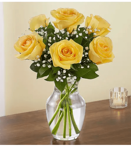 Yellow rose bouquet with baby's breath in a clear glass vase on a wooden table