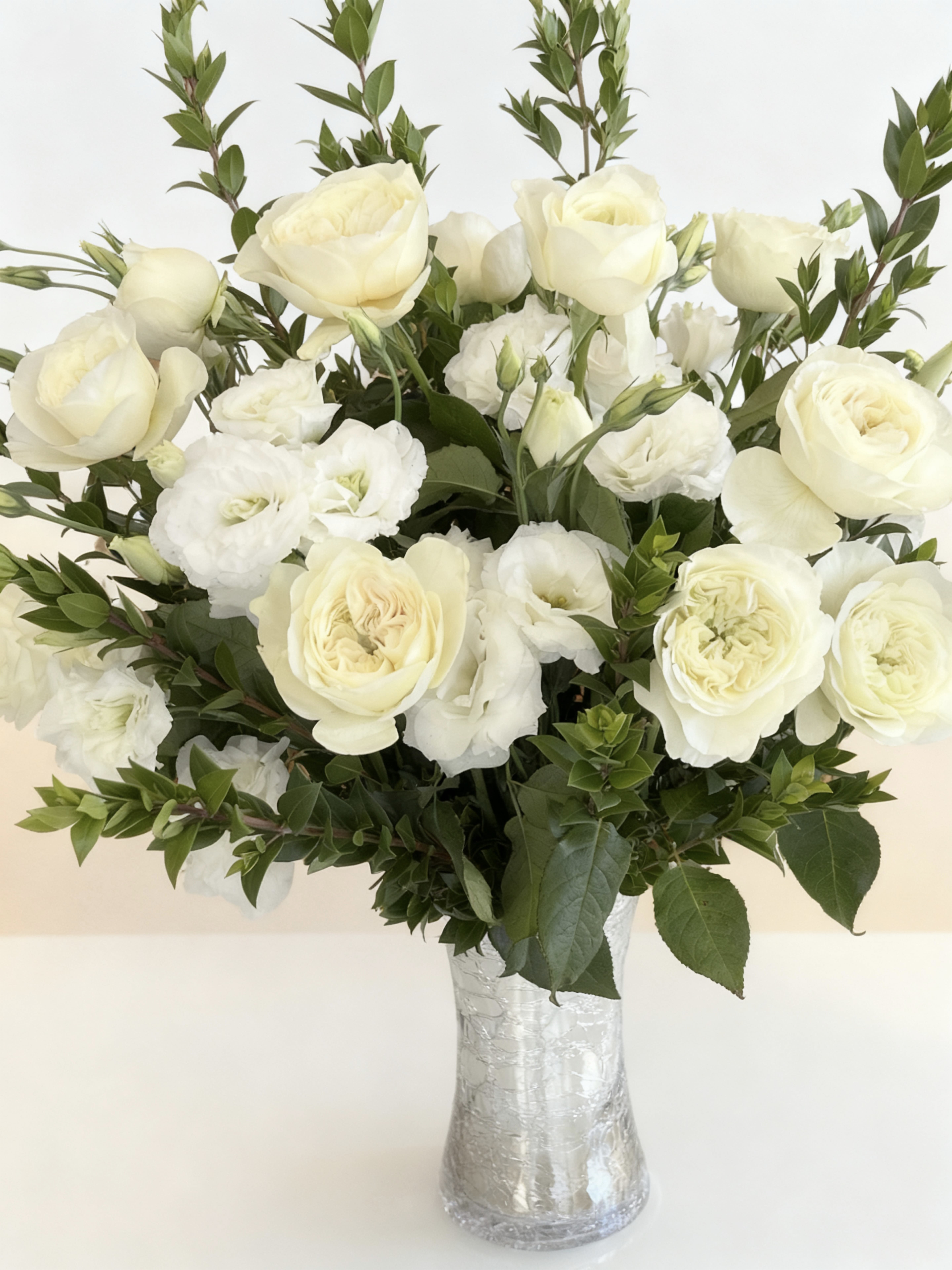 Lenora - 2 dozen LLenora Garden Roses &amp; White Lisianthus  Softly romantic and exquisitely refined, this arrangement pairs Lenora garden roses with delicate white lisianthus, creating a composition of effortless elegance and timeless beauty. Lenora roses are cherished for their full, ruffled blooms and gentle blush-champagne tones, opening into graceful rosettes that feel both luminous and inviting.  Interwoven among the roses, white lisianthus adds a light, airy contrast—its satin petals and graceful lines lending movement, softness, and a sense of modern refinement. Together, the florals create a balanced harmony of texture and tone: lush yet restrained, romantic yet elevated.  Hand-selected and artfully arranged, this design is ideal for meaningful celebrations, refined interiors, or moments that call for understated luxury. A poetic expression of grace and sophistication, it speaks quietly—but leaves a lasting impression.