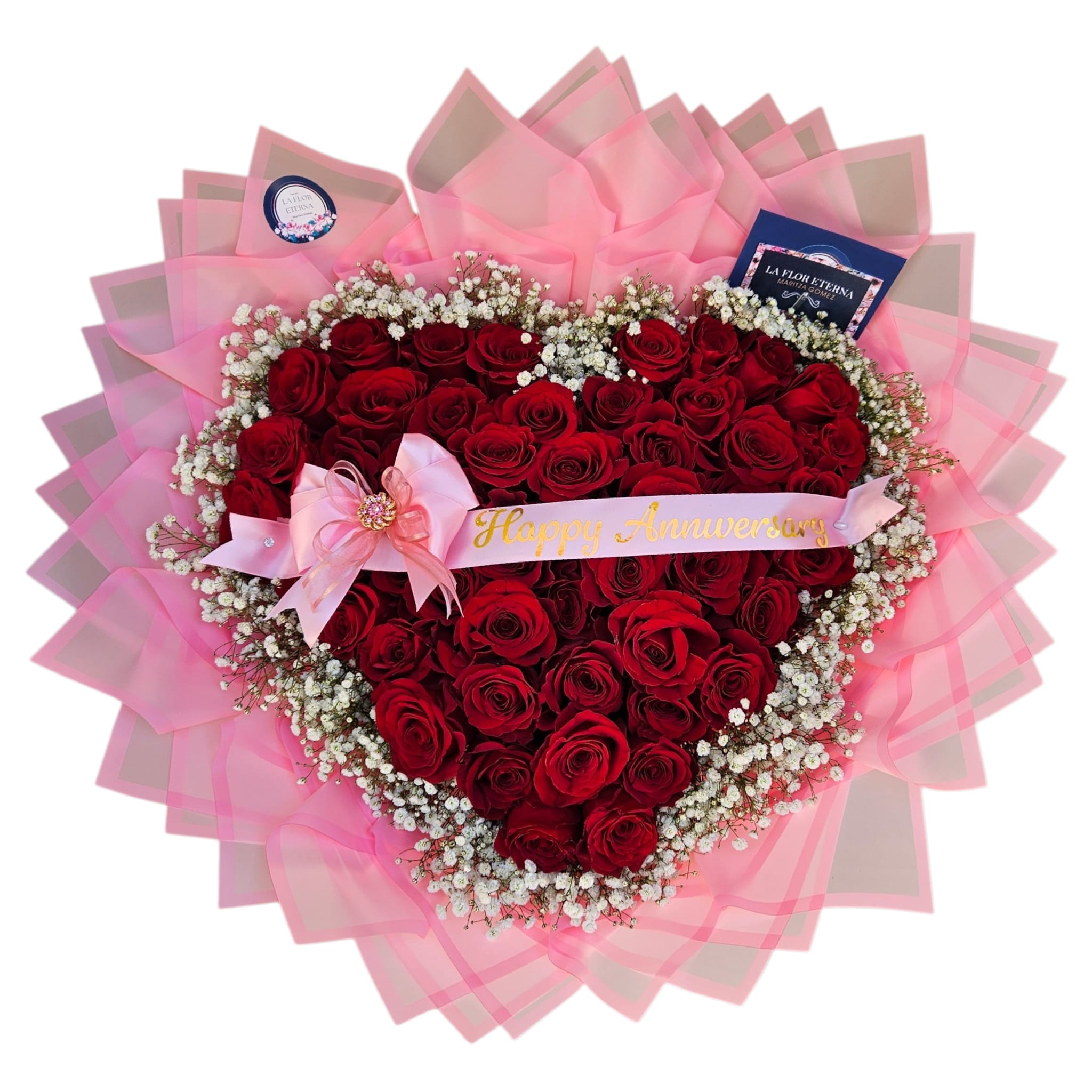 My Heart  - A dense heart of deep red roses framed by a ring of delicate white filler creates an immediate romantic statement - a heart-shaped flower arrangement made for anniversaries, Valentine's Day, or any love-themed celebration. The rich red center reads as timeless devotion, you can add pale pink ribbon and printed "Happy Anniversary"  banner across the heart make the message unmistakable; the person you're surprising will feel truly seen and cherished the moment they open it.  The arrangement sits on layered pink translucent wrap that fans outward like a ruffled border, giving the piece a soft, wearable texture and a glowing backdrop for the blooms. Deep red roses form the compact heart, white filler flowers provide a gentle contrast.  This lush, romantic silhouette arrives ready to display - an elegant way to mark anniversaries, romantic milestones, or to say "I love you" with classic floral drama. 