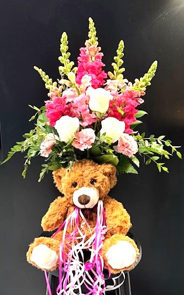#A011 - Sugar, Spice, &amp; Everything Nice! - Soft pink snapdragons and creamy white roses rise in a tall, vertical spray behind a cuddly brown teddy bear-this flower arrangement and plush gift set is perfect as a birthday bouquet or a new baby celebration. The bright pink spikes frame the ivory roses while long strands of curled pink and white ribbon cascade over the bear's lap, creating a playful, youthful display that feels affectionate and joyful.   Includes carnations, roses, and snapdragons in a mix of pink and white, and greenery for a cheerful, mixed-color palette. The arrangement's vertical shape gives it presence on a table or hospital room stand, and the attached teddy bear adds a keepsake touch that comforts and delights. Ideal for welcoming a newborn, brightening a bedside, or sending a sweet birthday surprise-the recipient will feel truly seen and celebrated. 