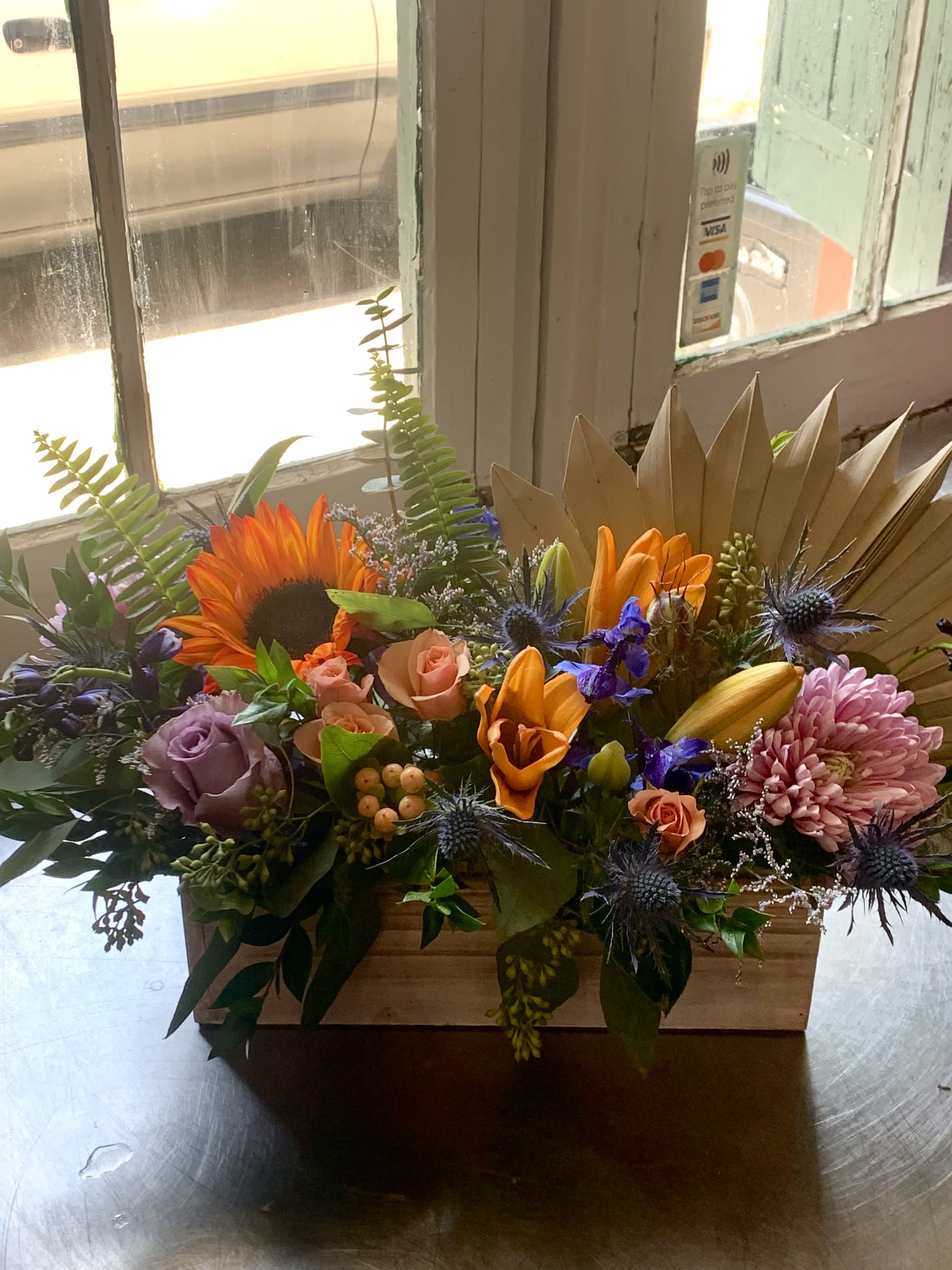 Mixed floral arrangement in a wooden box with sunflowers, roses, and lilies