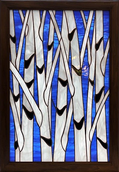#A030 - Summer Birches - Stained Glass Window - A vertical stained-glass panel framed in dark wood transforms sunlight into a tranquil forest scene-perfect as a Mother's Day gift or a thoughtful housewarming present. This home décor item reads like artful foliage: slender white birch trunks in pearly, marbled glass rise against deep cobalt blue, the contrast creating a calm, modern focal point that will make the recipient feel seen and soothed. Crafted with a wooden frame and a stained-glass panel, the design uses overlapping, stylized birch trunks with small black accents that suggest natural knots-clean lines and layered depth give it a contemporary, gallery-ready look.   Sized to hang in a window or on a wall, it functions as both light-filtering art and an enduring keepsake that outlives cut flowers. Give this as an anniversary or birthday gift to someone who loves nature and clean design, or as a "just because," thank you, or retirement piece that brings serenity to a home office or living room. It also fits seasonal moments-spring and summer light play beautifully through the cobalt background-making it a versatile choice for Father's Day, graduation, wedding or holiday giving when you want a lasting, meaningful present.