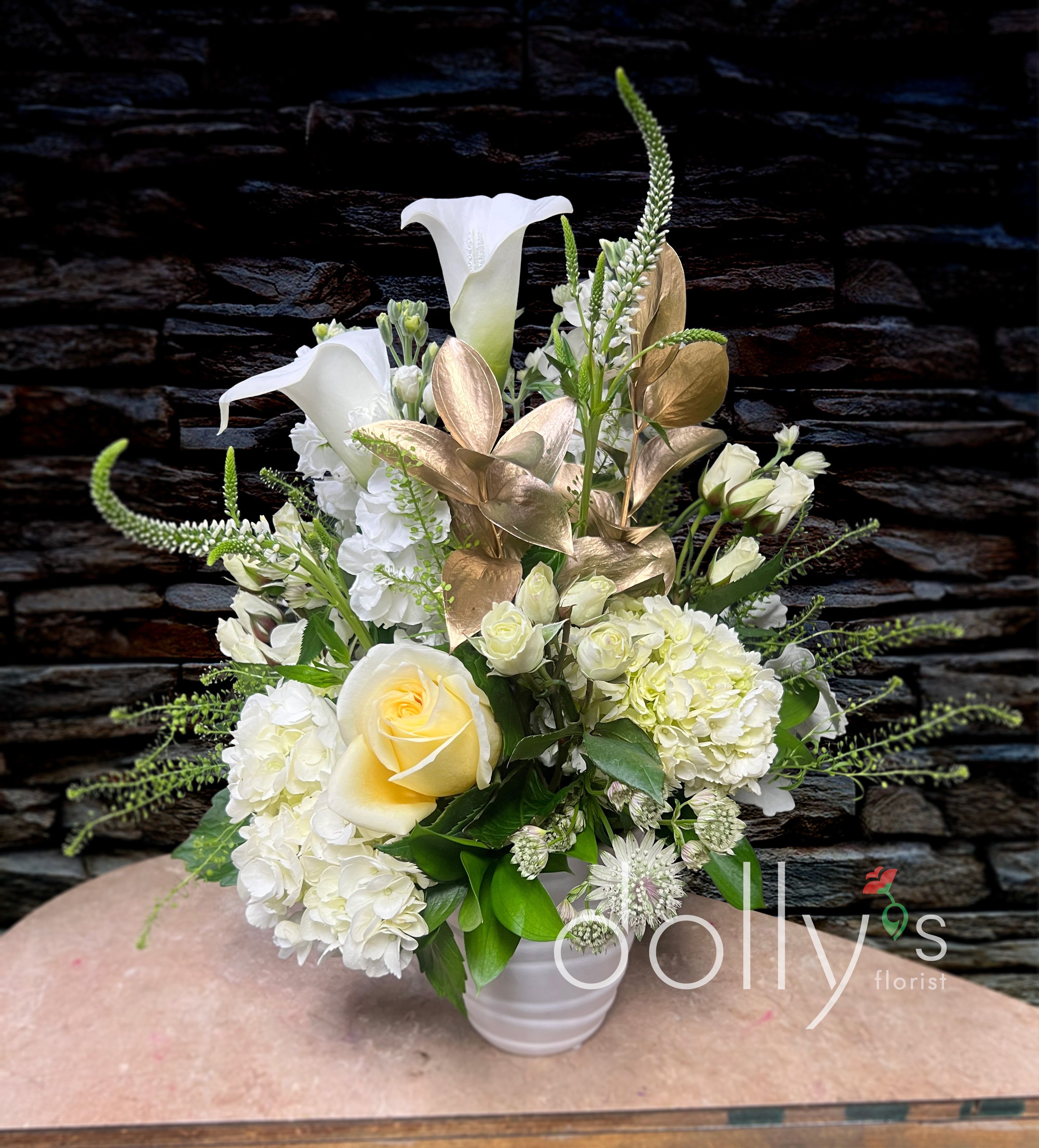 New Beginnings - Composed of a bright white palette of calla lilies, hydrangeas, and spray roses accented with gold ruscus. 