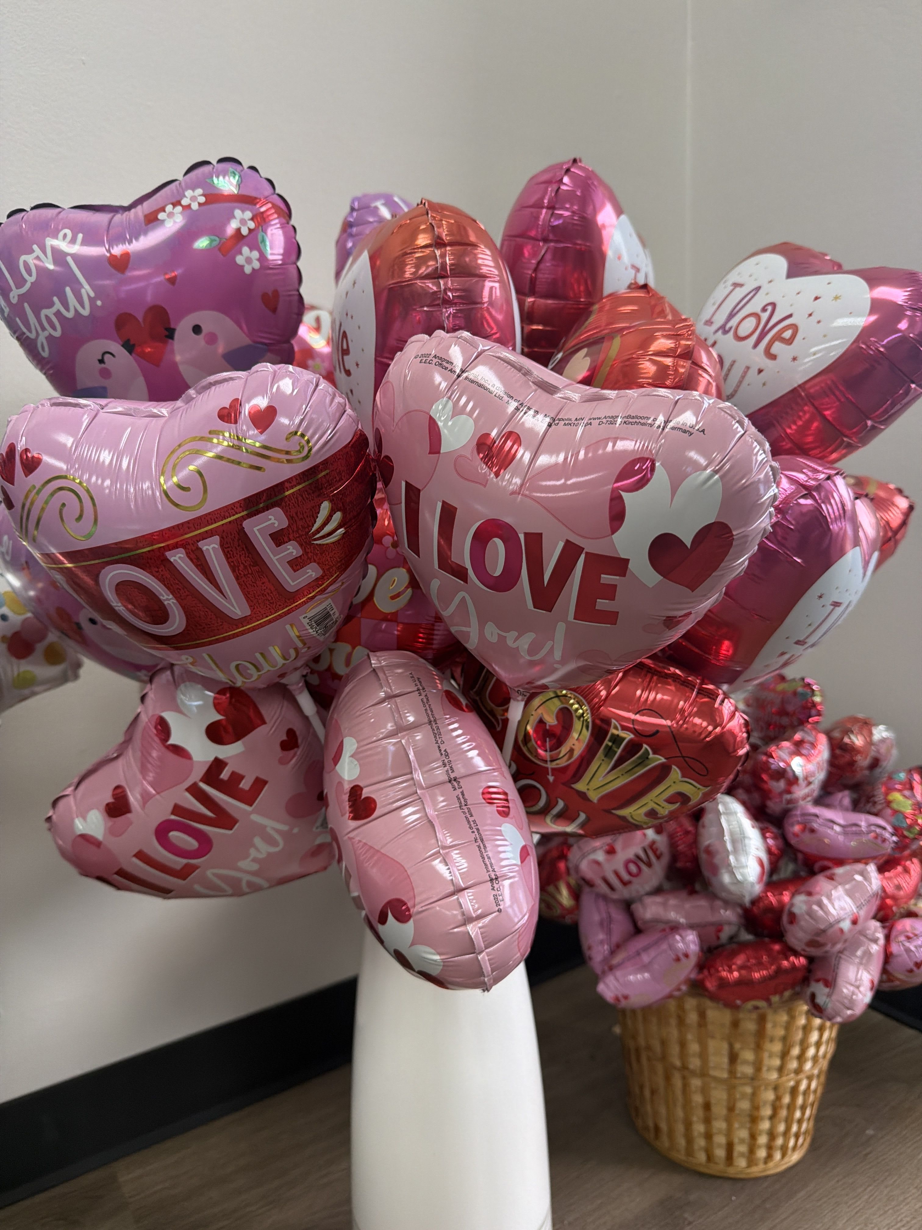Heart-shaped pink and red balloons with love messages in a white vase and basket