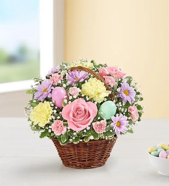 Easter Egg Basket™ - A delightful way to deliver Easter wishes. We’ve gathered fresh-picked pastel blooms and colorful eggs inside a charming handled basket. It’s a gift of instant happiness for family and friends, both near and far.  All-around arrangement with light pink roses, pink mini carnations, yellow carnations and lavender daisy poms; accented with baby’s breath, assorted greenery and colorful plastic Easter eggs Artistically designed in a handled basket with liner; measures 6"H