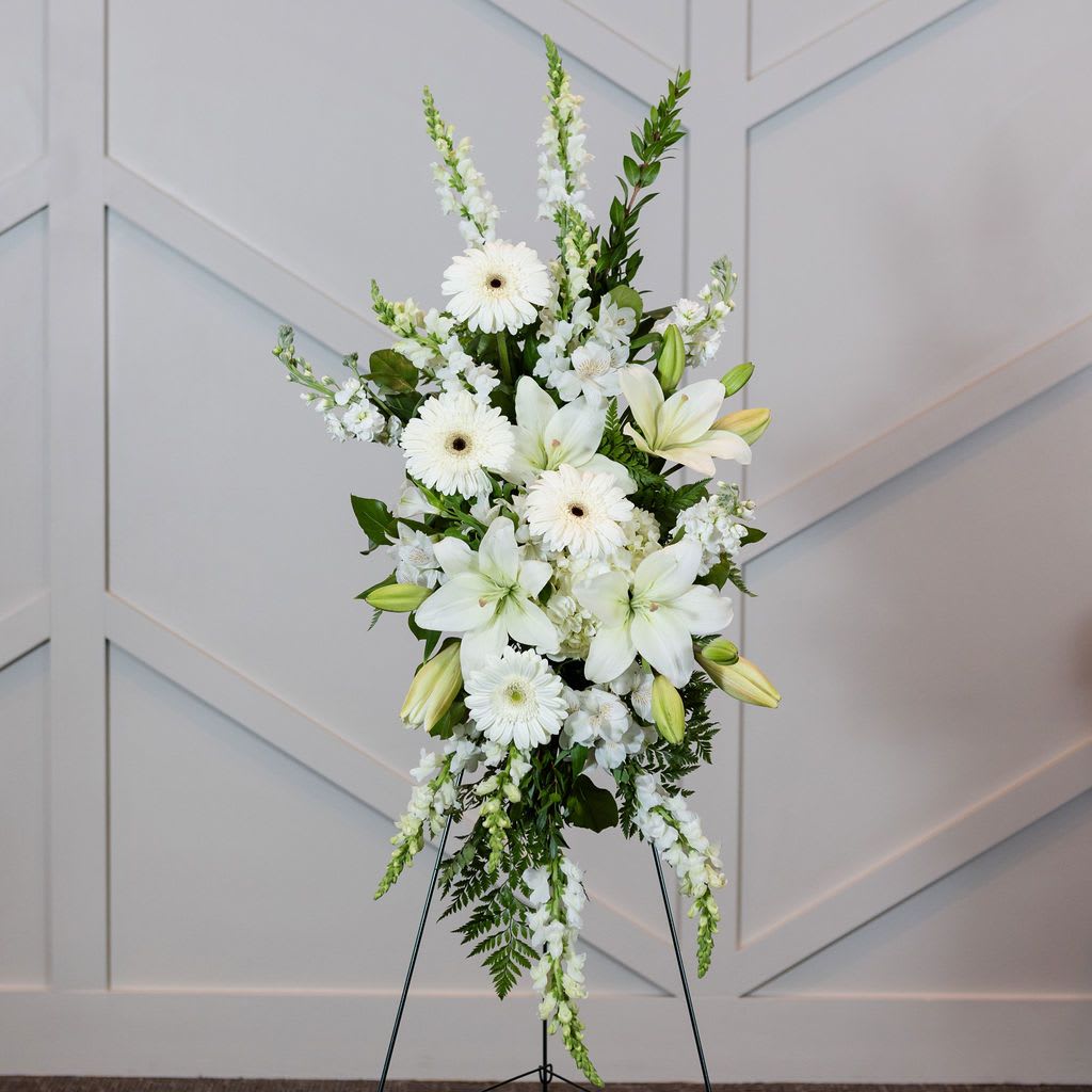 White floral standing spray on an easel with lilies and daisies
