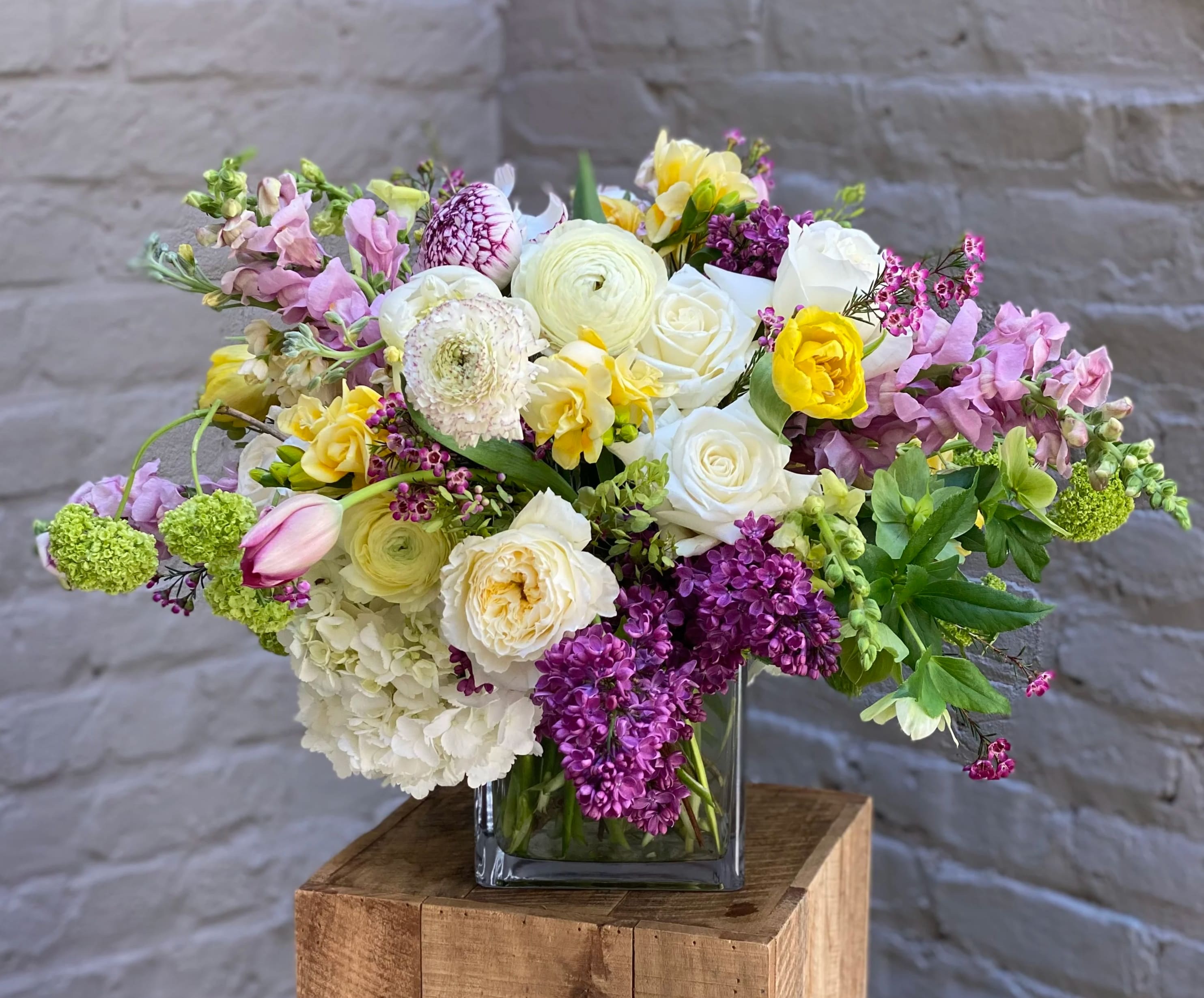 Caroline - Named to honor the mother of one of our long-time delivery drivers, Caroline is a gorgeous arrangement fit for a queen.  Local-grown ranunculus and fragrant freesia dance with cascades of local lilac, creating a grand statement of opulence that mirrors the finest royal gardens in springtime.