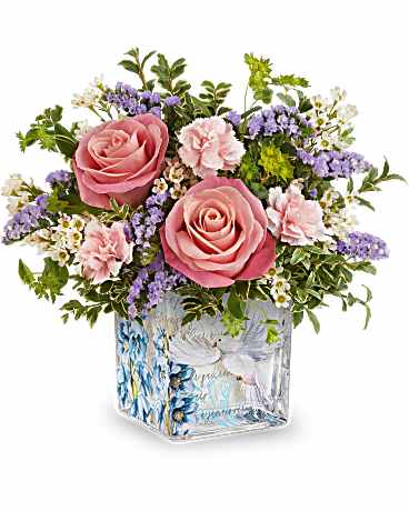 Whispers of Grace - Soft pink roses anchor a low, rounded arrangement that reads like a gentle embrace - perfect as a Mother's Day bouquet, a sympathy tribute, or a thoughtful just-because gift. Pastel pink carnations, clusters of tiny white blooms and lavender-purple fillers weave through the roses, while touches of blue lend a cool, calming lift. The dove-and-blue-floral printed square glass vase reinforces the serene, hopeful feeling, making this arrangement especially fitting for Easter, Passover, or occasions that call for comfort and grace.  Compact and closely gathered, the blooms form an intimate, textured dome that sits neatly atop the decorative square vase; the design works well for bedside, mantel, or kitchen table display. Ideal for birthdays, get-well wishes, thank-you gestures, housewarmings, Earth Day or Best Friends Day celebrations, and moments when you want the person you're thinking of to feel quietly seen and cared for. Care: keep water fresh and trim stems every few days to extend vase life.
