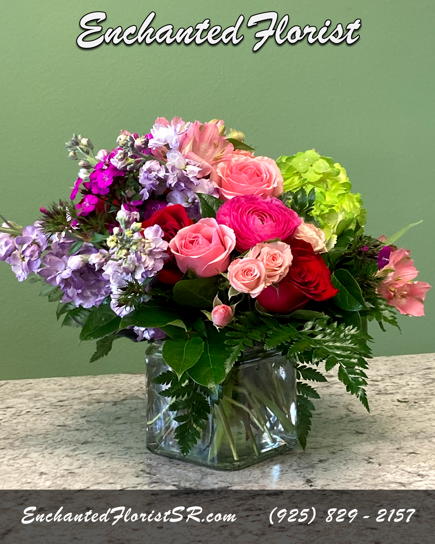 Mixed arrangement of pink and red roses with purple flowers in a clear glass cube vase
