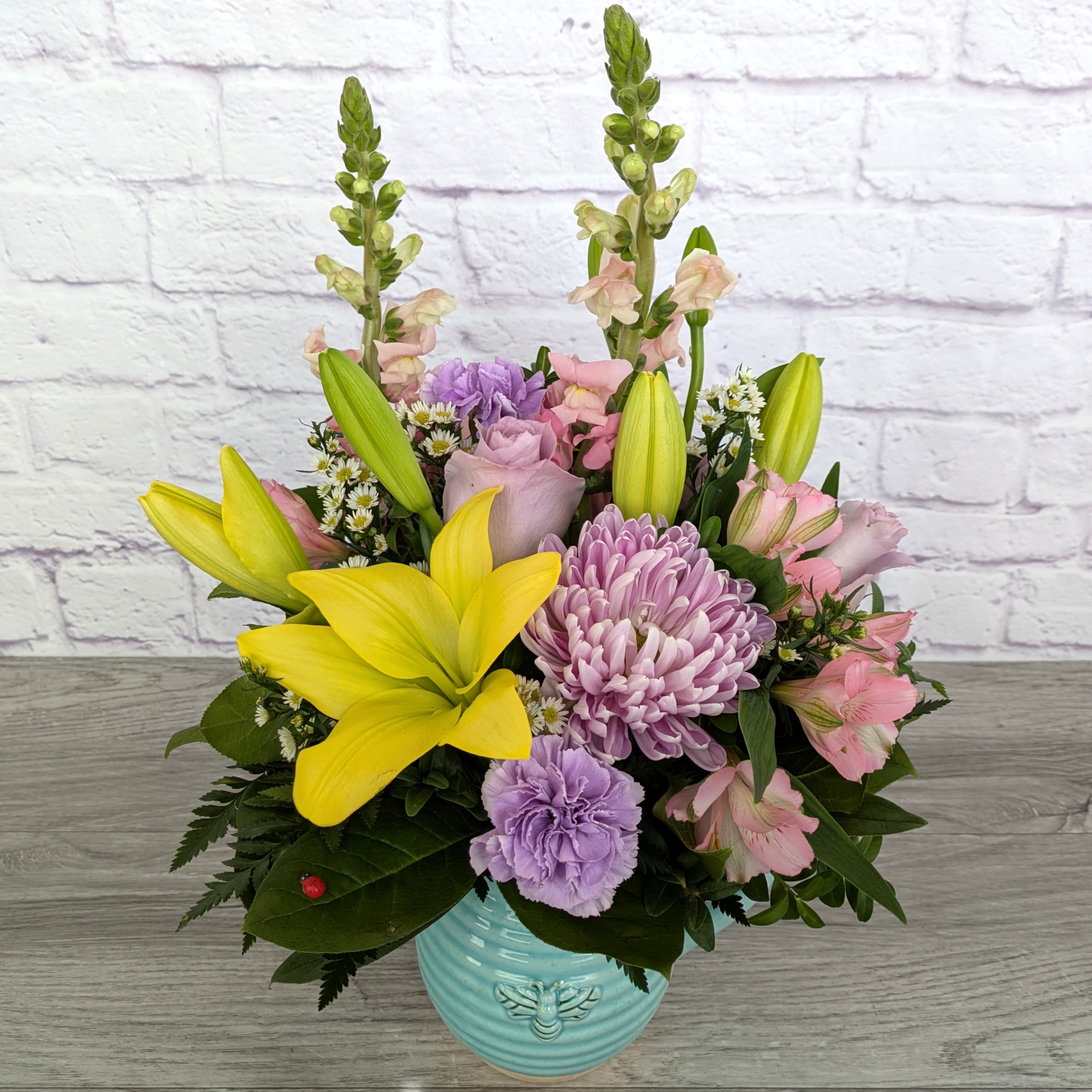 Beeautiful Pitcher - Beeautiful Pitcher is A Ladybug Floral exclusive bouquet. This bouquet features asiatic lilies, snapdragons, football mums, alstroemeria, roses, carnations and monte casino. Featured in a teal artisan ceramic pitcher with an embossed bee motif.  Orientation: All Around 20” Tall 14” Wide  