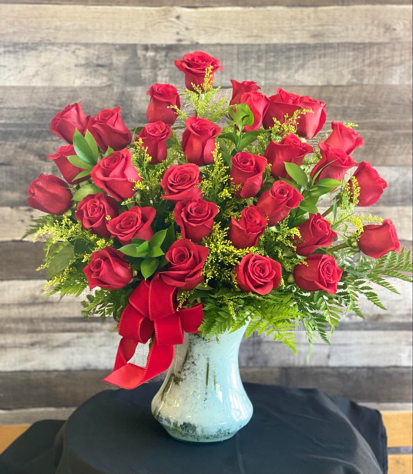 Red roses arranged in a blue glass vase with a red ribbon