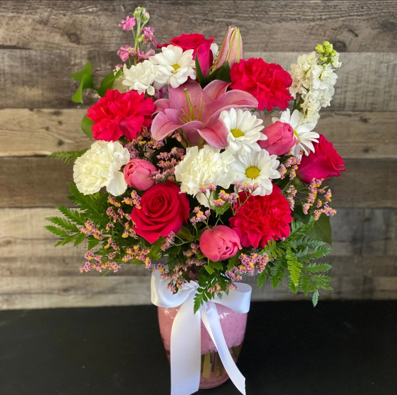 Mixed bouquet of pink, red, and white flowers in a pink vase with a white ribbon