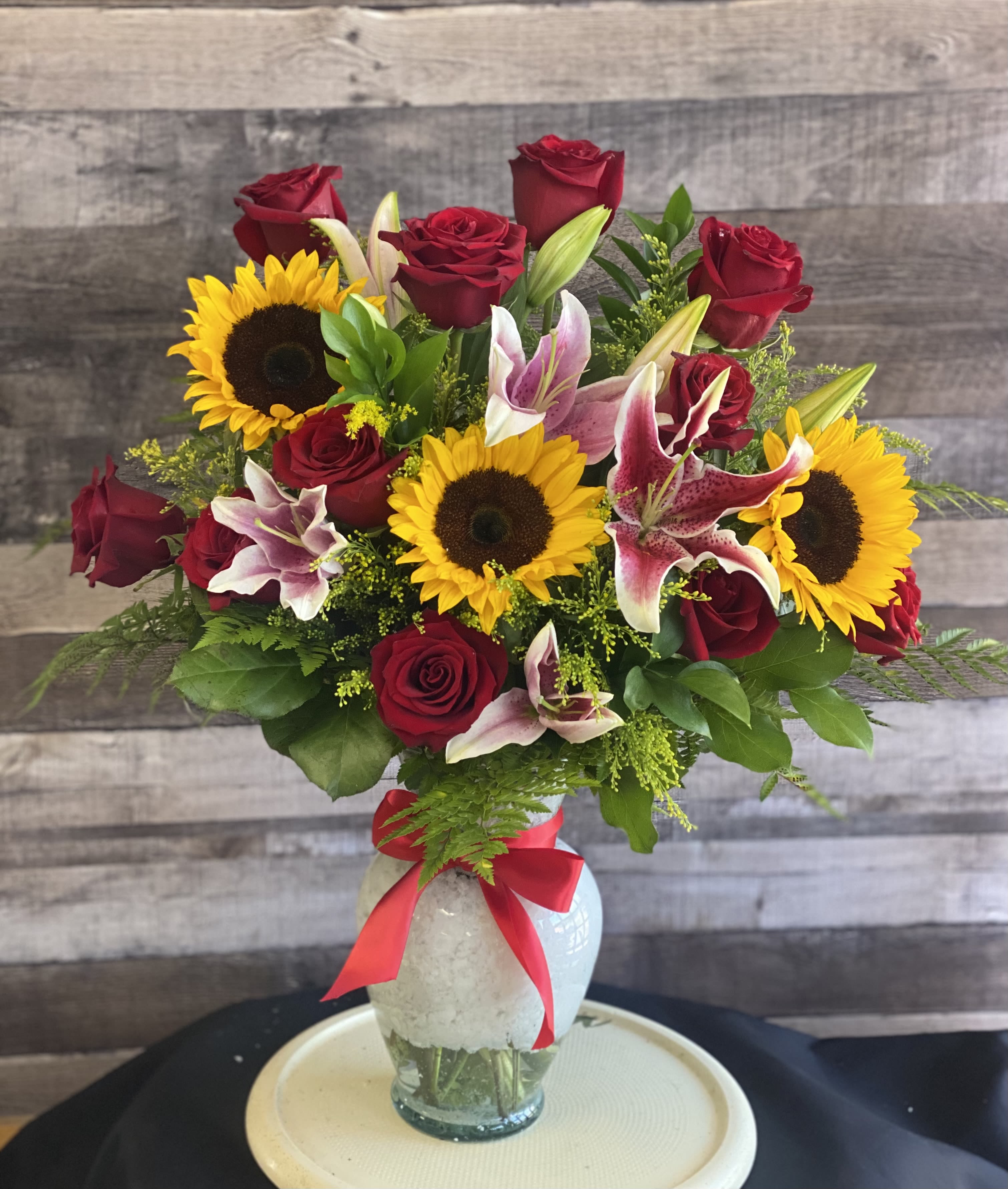 Bouquet of red roses, sunflowers, and lilies in a glass vase with a red ribbon