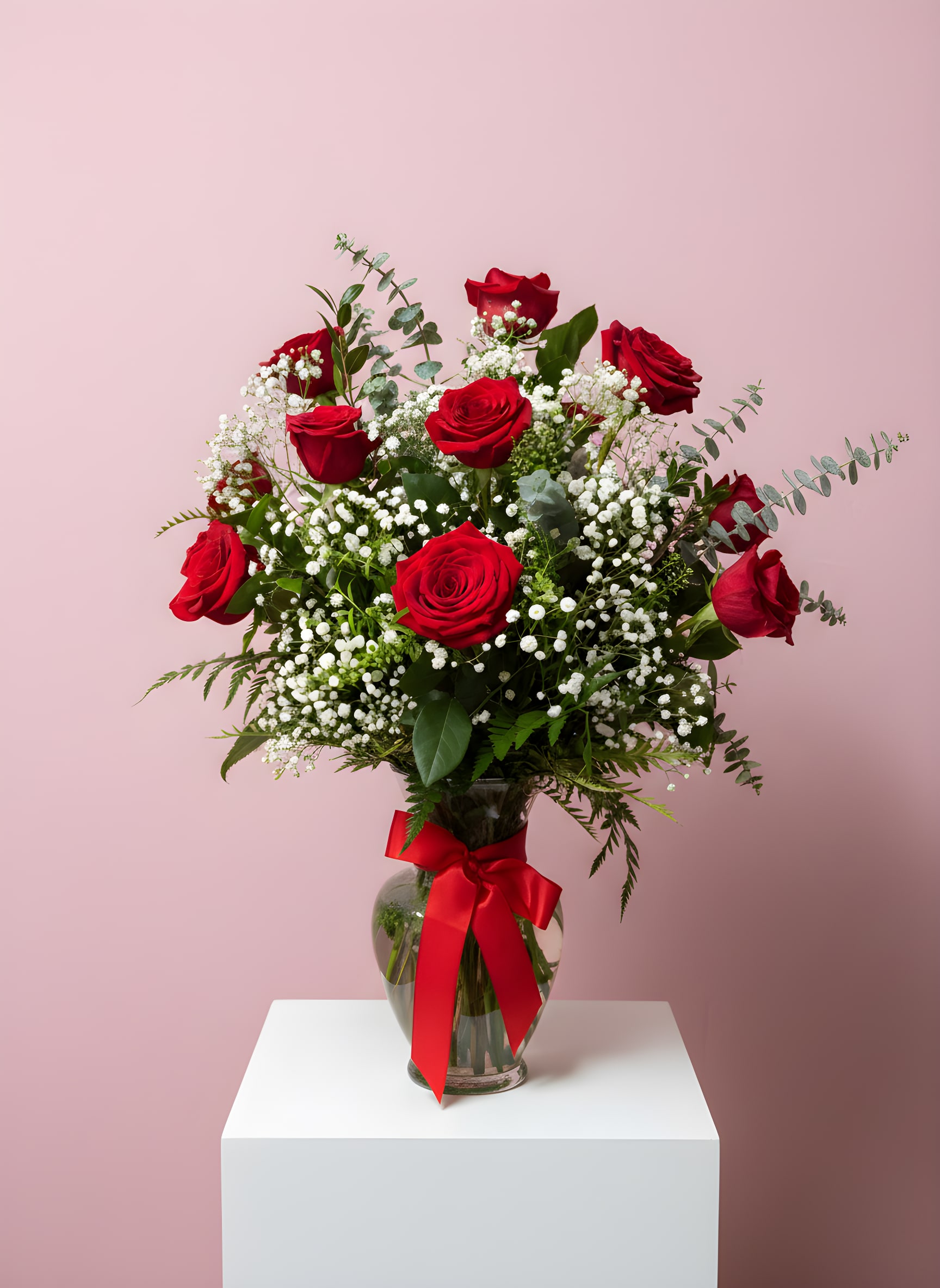 Red roses in a glass vase with baby's breath and a red ribbon