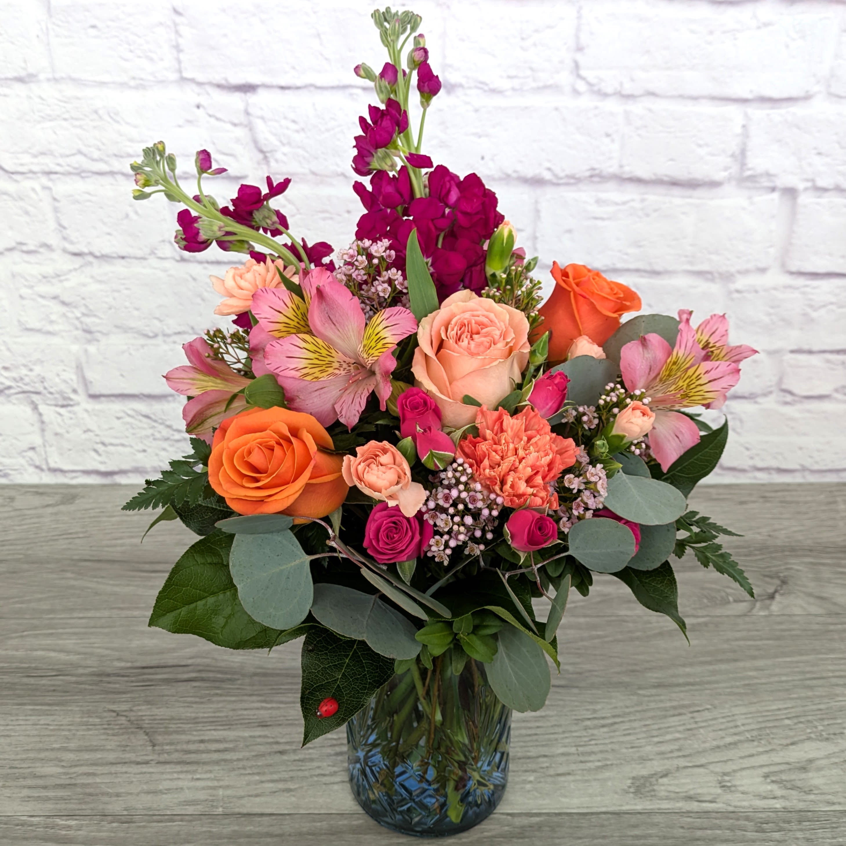 Peach Harvest - Peach Harvest is A Ladybug Floral exclusive bouquet. This bouquet stock roses, spray roses, alstroemeria, carnations, mini carnations, wax flower and silver dollar eucalyptus. Featured in a 6.5” sculpted blue glass vase.  Orientation: All Around 17” Tall 13” Wide  