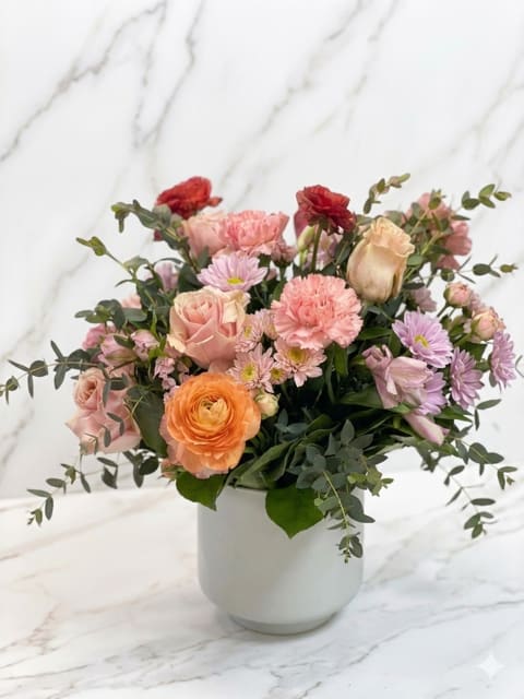 Love's Bounty - This lush arrangement features delicate blush pinks, creamy peaches, and rich pops of burgundy, all nestled in fresh greenery. Designed with a loose, garden-inspired style.
