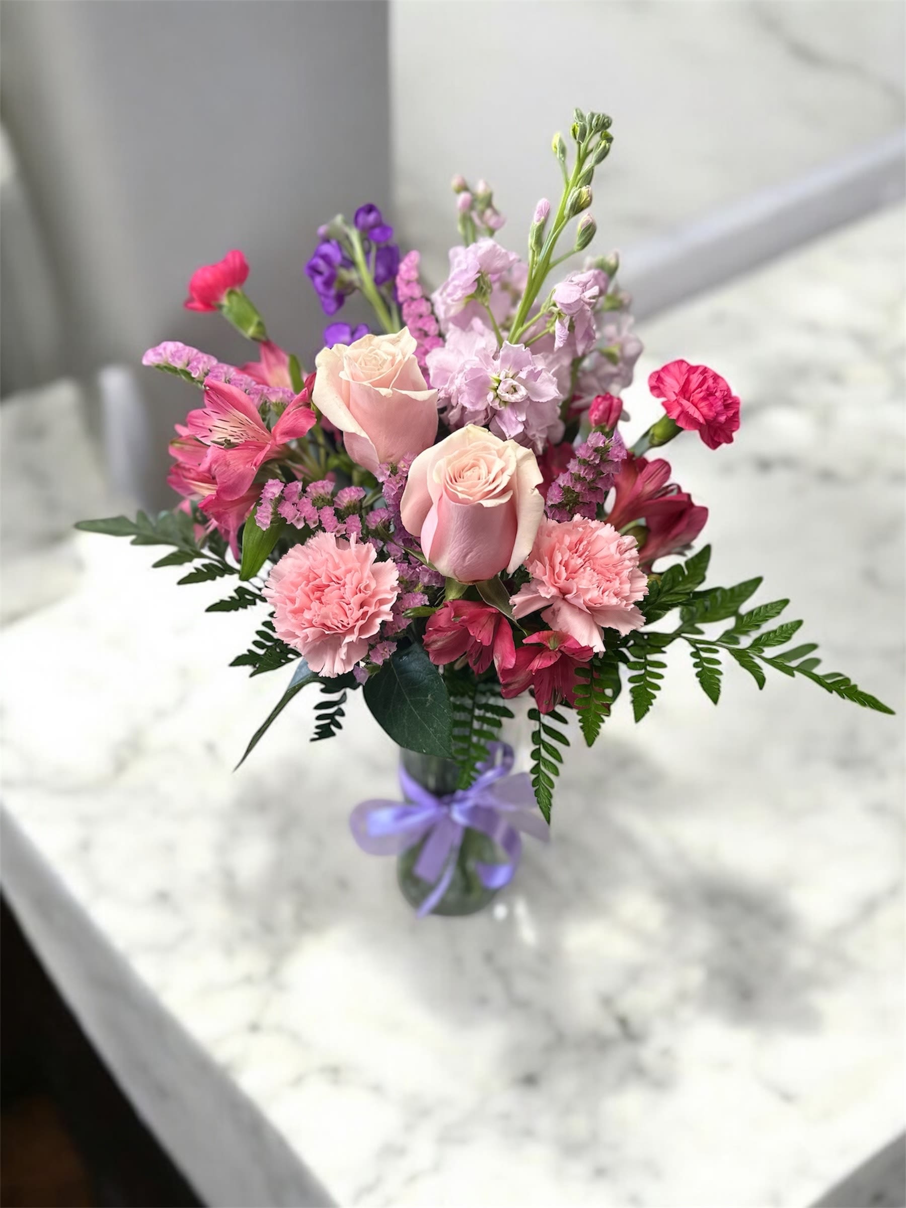 Pink and purple mixed bouquet in a glass vase with a lavender ribbon