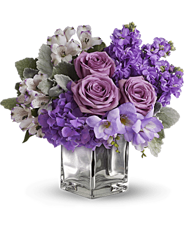 Purple and pink floral arrangement in a clear square vase