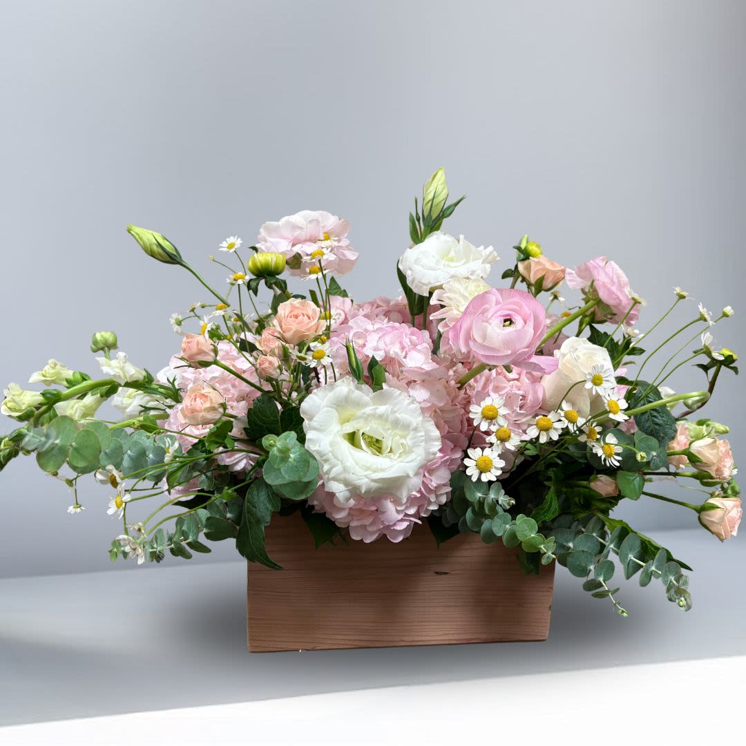 Celebrating Engagement - Recipe: Hydragaes, Snapdragon, Lisianthus, Roses, Baby Breath, Greens in a local hand-made wooden box. Availability: Seasonal Ranunculus Dimensions: Center piece in wooden box. 11" long regular 14" long premium 