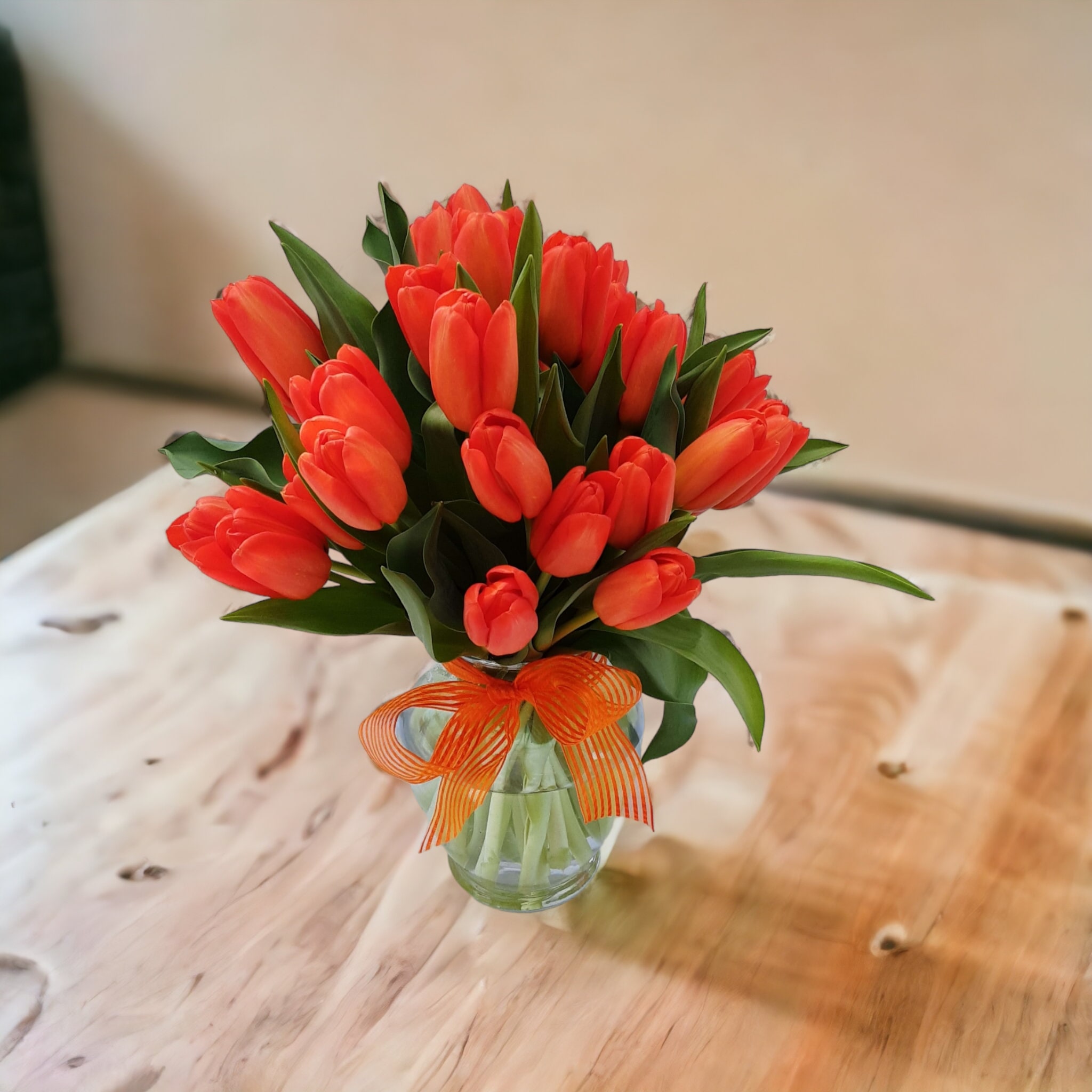 Bouquet of orange tulips in a clear glass vase with an orange ribbon