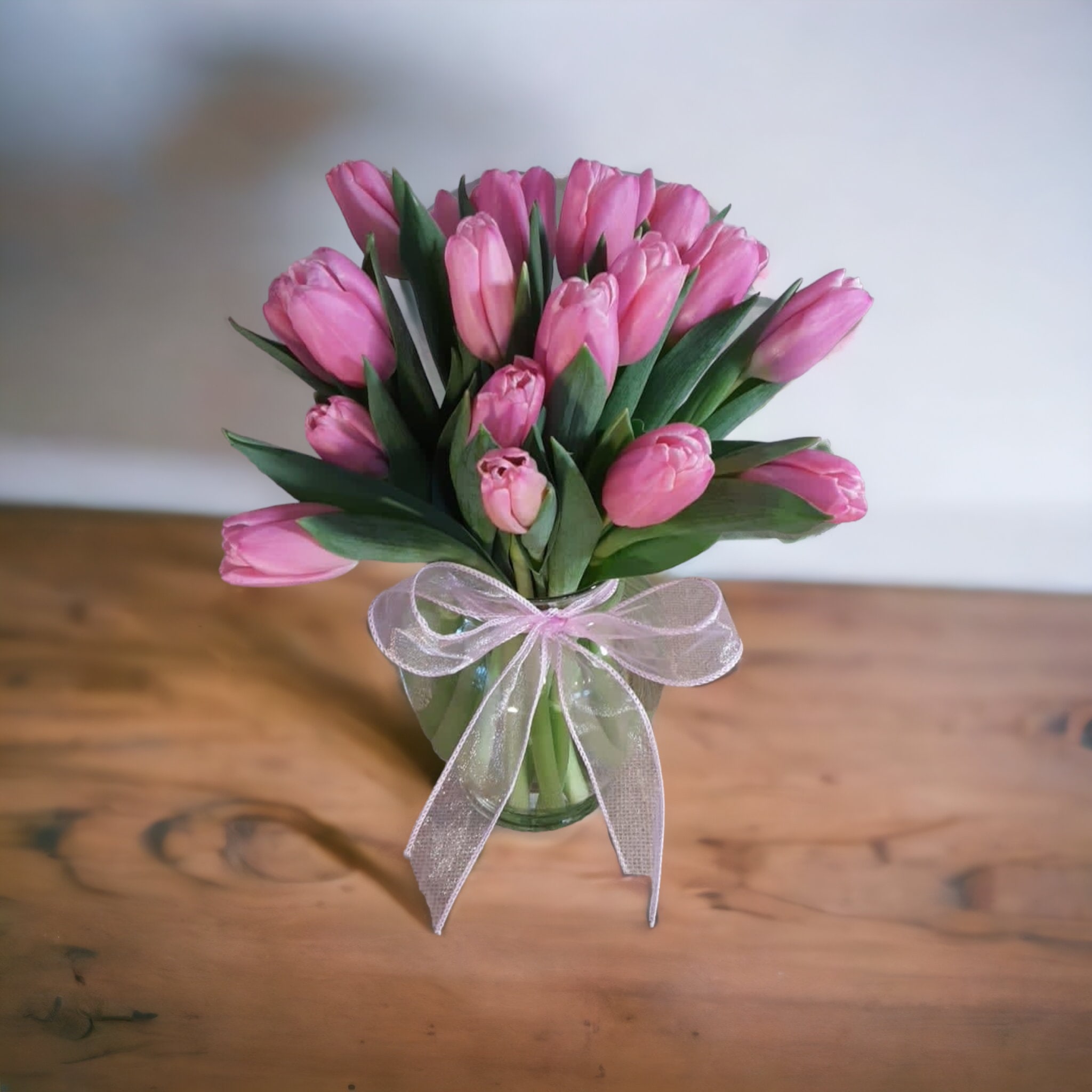 Pink tulips in a clear glass vase with a sheer ribbon