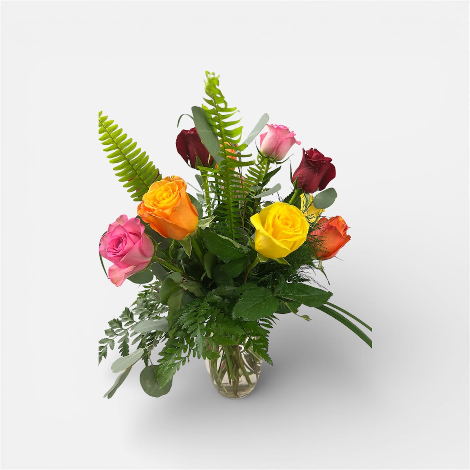 Melody of Roses - A bright cluster of red, yellow, pink, and orange roses arranged in a clear glass vase-Melody of Roses is a cheerful flower arrangement perfect for birthday bouquets, congratulations, or simply letting someone know you're thinking of them. The lively mix of warm tones creates an uplifting, celebratory mood that will make the recipient feel noticed and genuinely celebrated.  Twelve assorted colored roses are gathered in a low, clear glass vase with textural mixed greens and upright fern fronds that add height and a sense of movement. Round silver-toned foliage provides a modern contrast to the smooth rose petals and helps each bloom stand out whether they're grouped tightly or spaced with airy gaps. The design reads as fresh and friendly, an easygoing yet polished choice for everyday gifting.  This arrangement is sized to sit comfortably on a table or desk and arrives ready to display-no extra trimming required beyond routine water changes. Choose Melody of Roses when you want a colorful, confident way to send affection, congratulations, or encouragement.