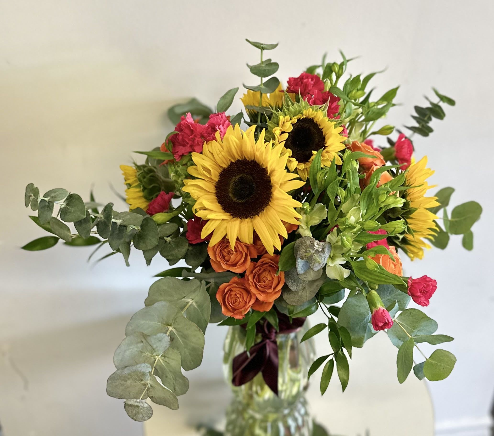 Bouquet of sunflowers, orange roses, and pink carnations in a glass vase