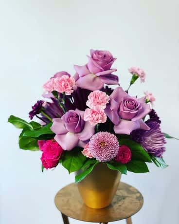 Purple and pink floral arrangement in a gold vase