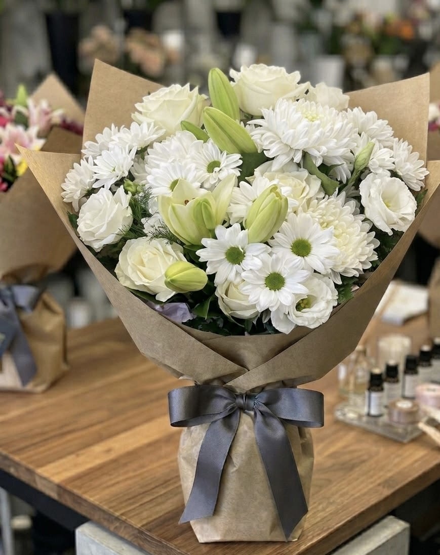 White bouquet with lilies, roses, and daisies wrapped in brown paper